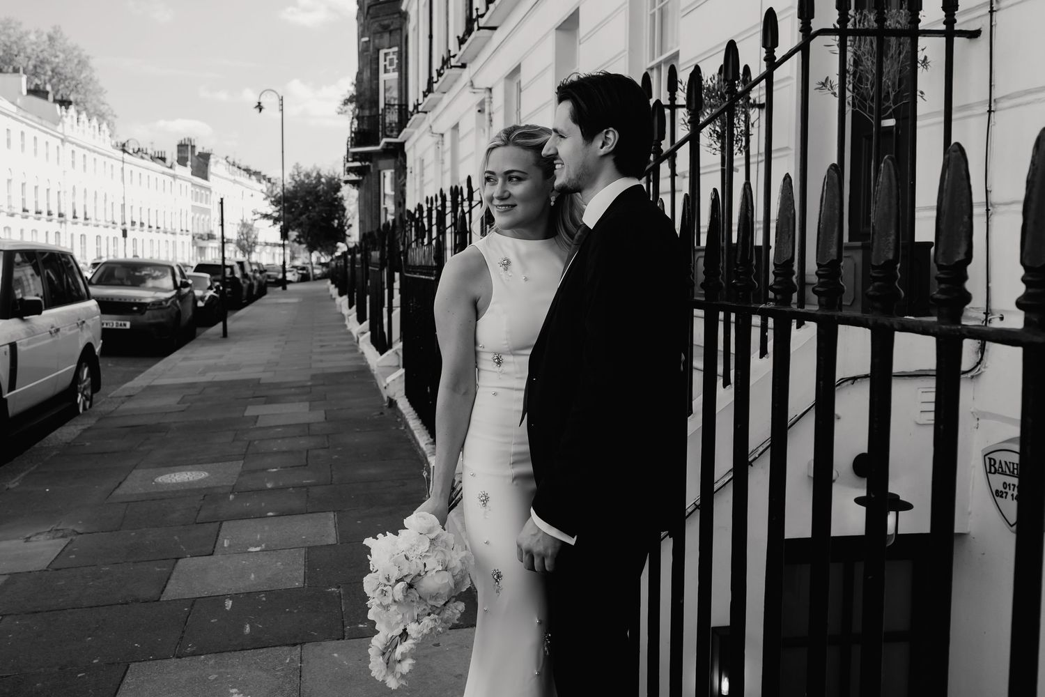 Elegant bride and groom walk along a classic London street lined with white Georgian townhouses.