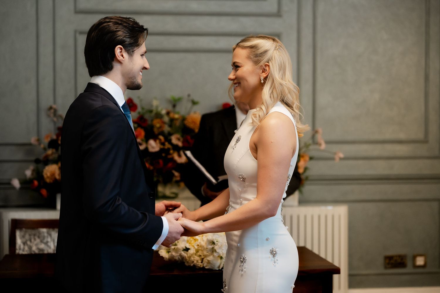 Bride and groom hold hands smiling at each other during intimate wedding ceremony exchange.