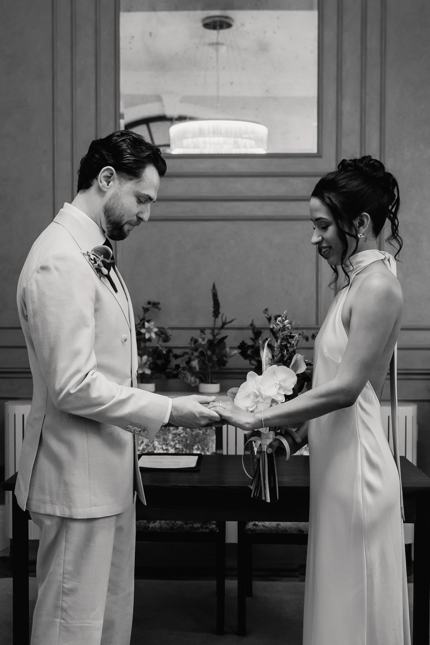Black and white photo of bride and groom exchanging rings during their elegant wedding ceremony.