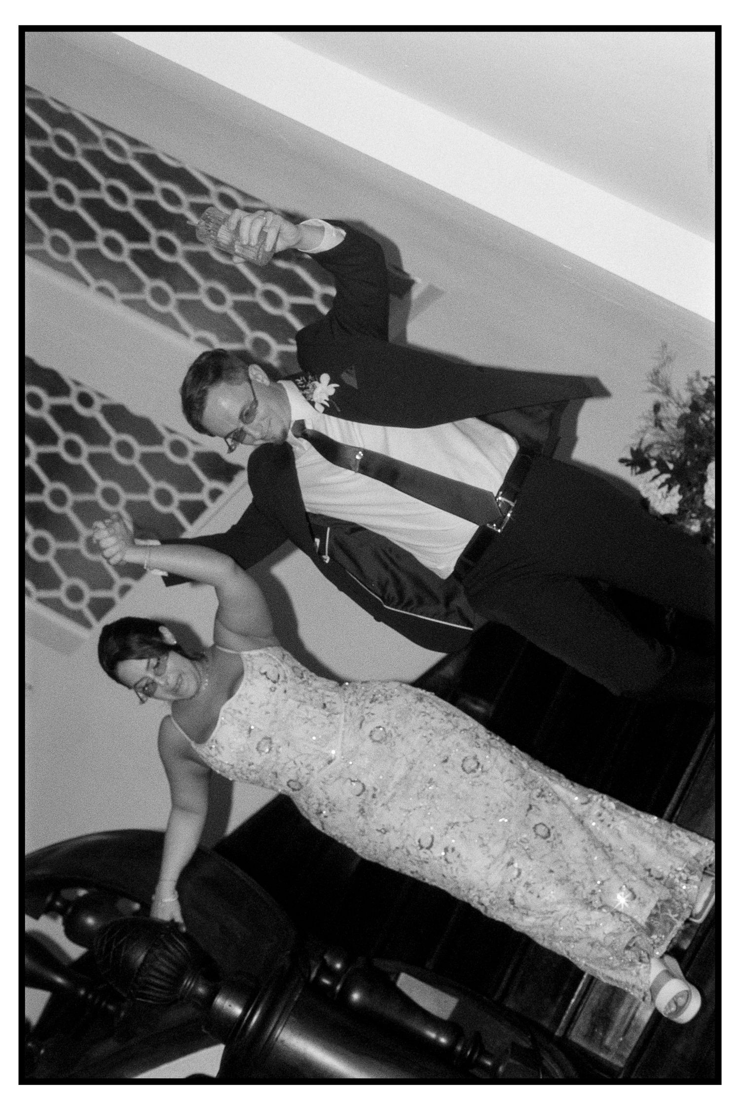 Black and white tilted photo of bride and groom dancing energetically at wedding reception.