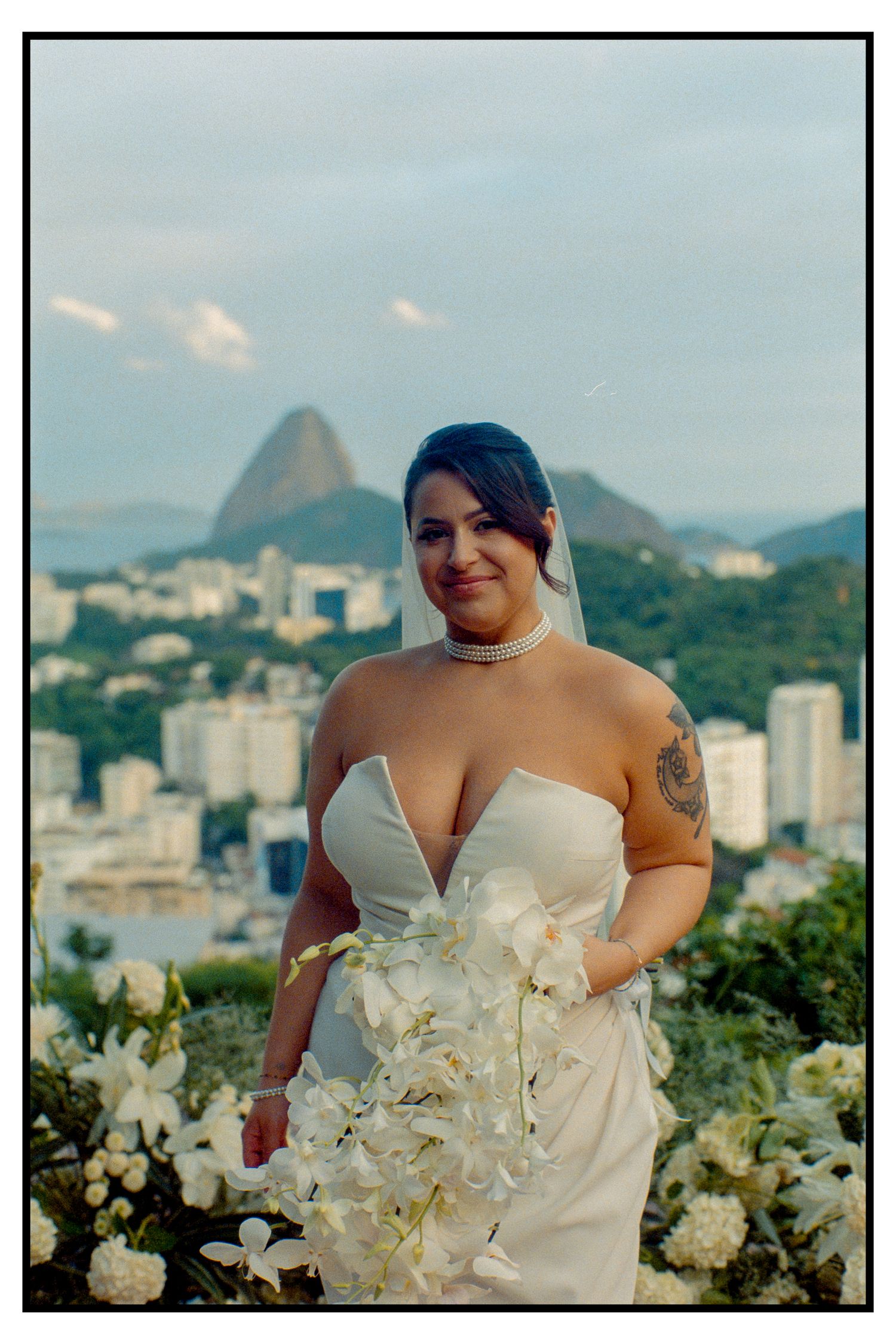 Beautiful bride in white gown holding orchid bouquet with Rio de Janeiro and Sugarloaf Mountain behind her.
