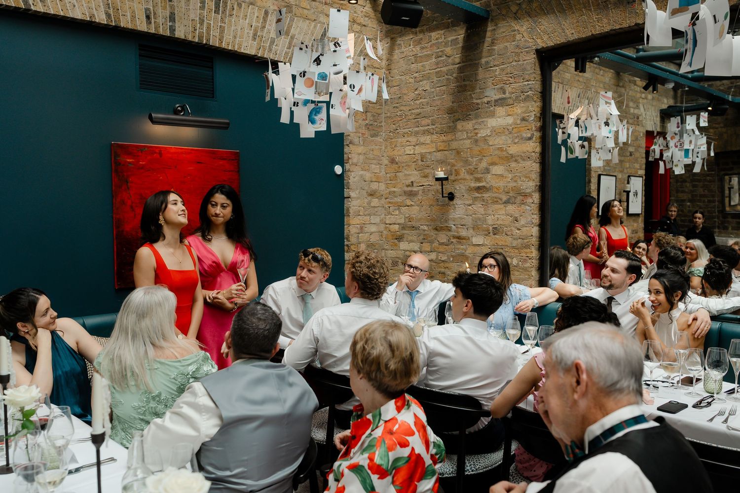 Wedding reception guests seated at tables with performers in red dresses entertaining.