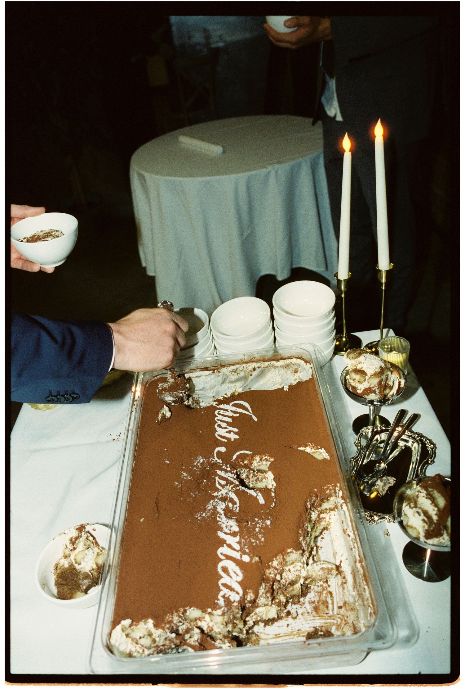 Wedding dessert table with partially served tiramisu cake, lit candles, and elegant serving dishes at reception.
