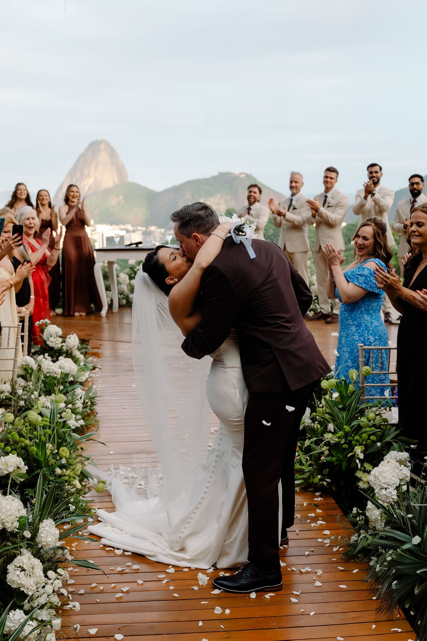 Bride and groom share first kiss at outdoor rooftop wedding ceremony in Rio de Janeiro with Sugarloaf Mountain backdrop.