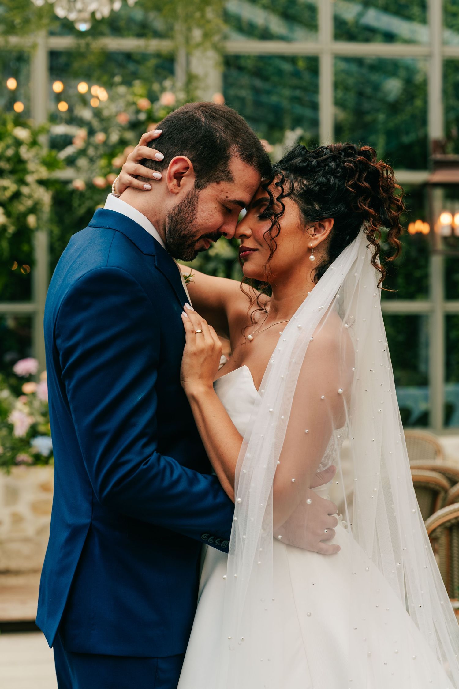 Bride and groom share an intimate forehead touch in a lush greenhouse wedding venue.