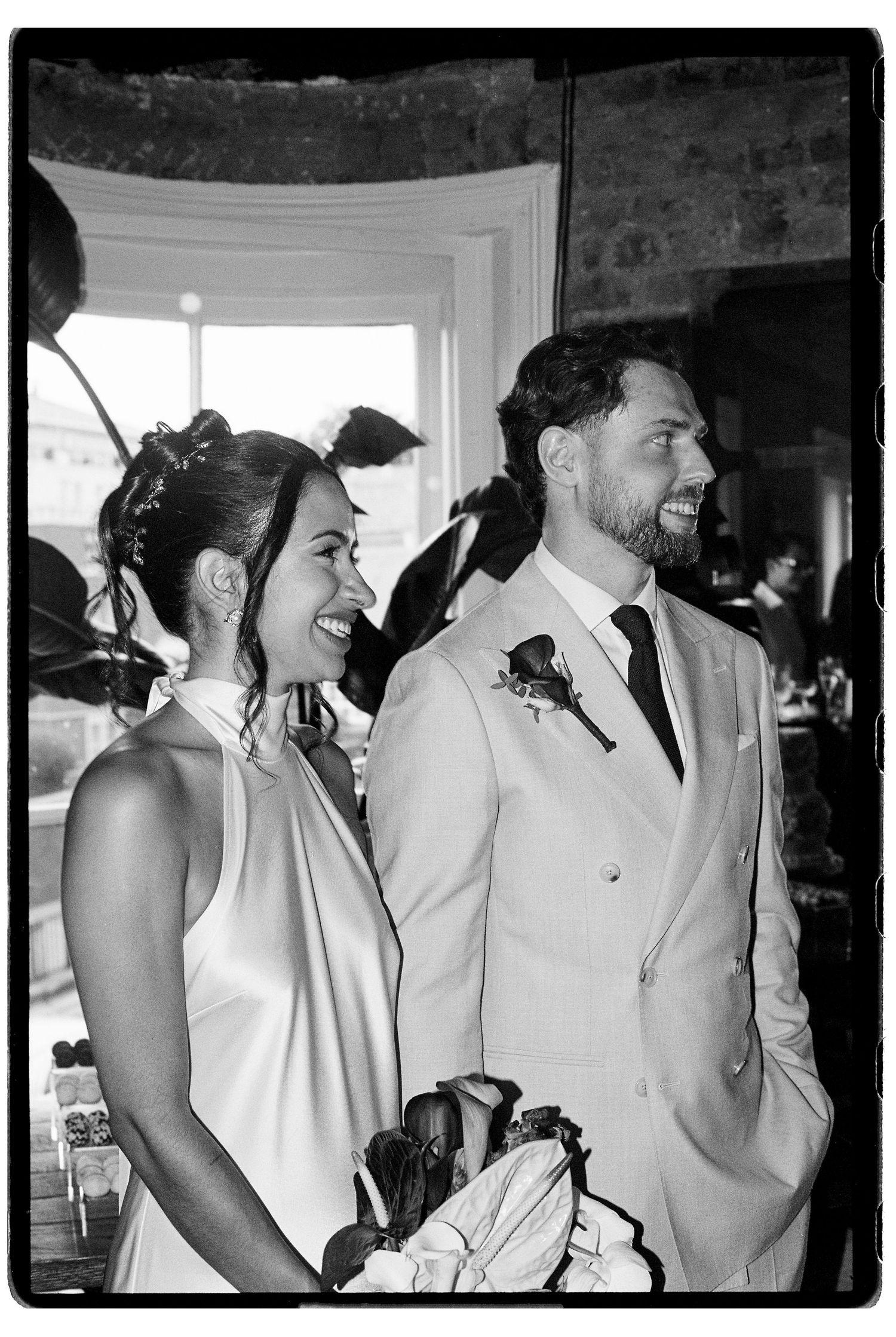 Black and white portrait of smiling bride and groom standing together during wedding reception indoors.