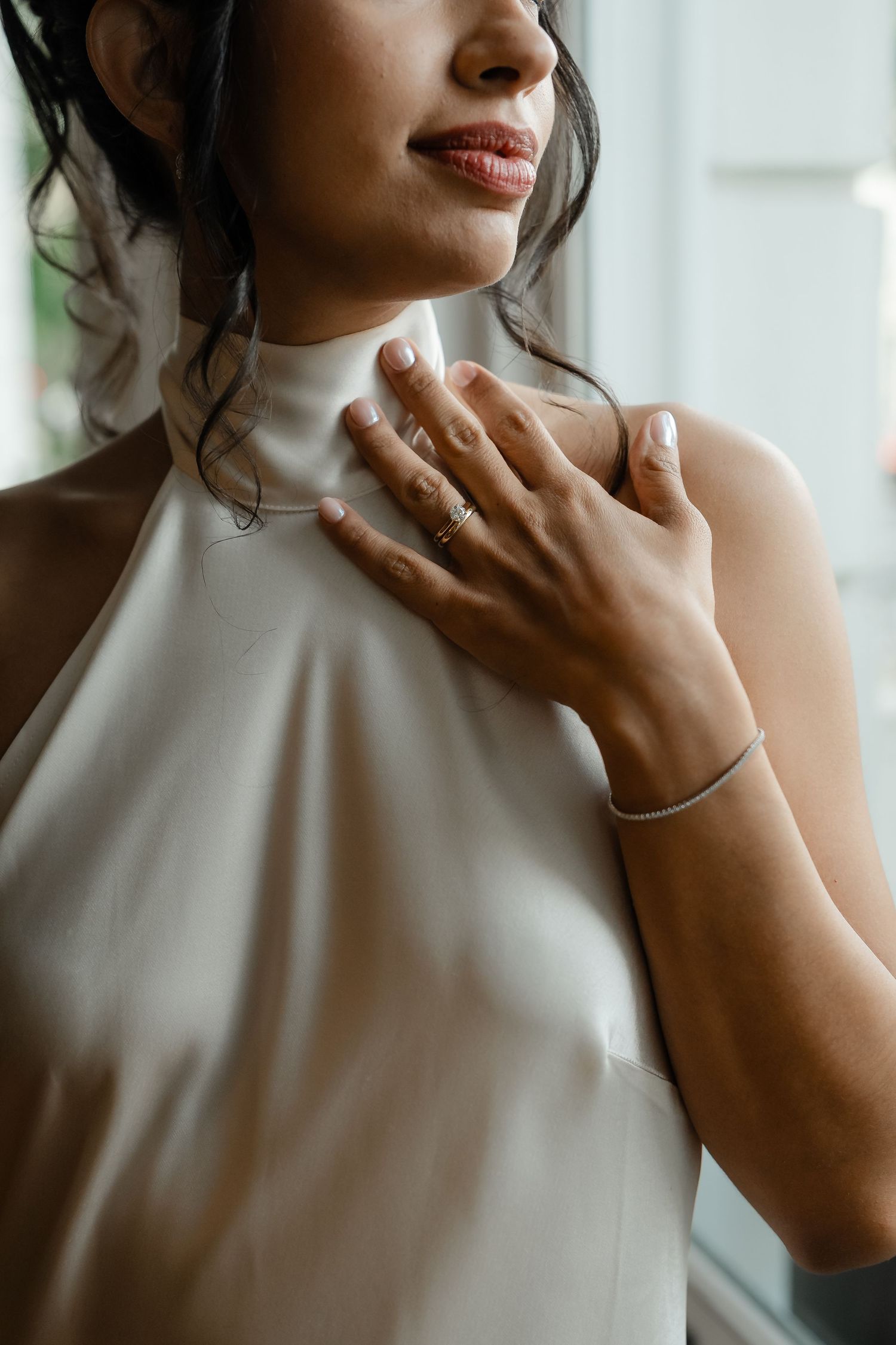 Close-up of bride in white silk halter dress with delicate jewelry and red lips on her wedding day.