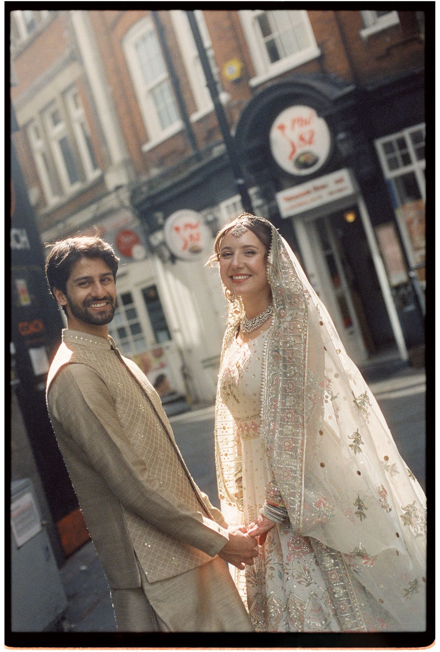 South Asian couple in traditional wedding attire holding hands on a London city street.
