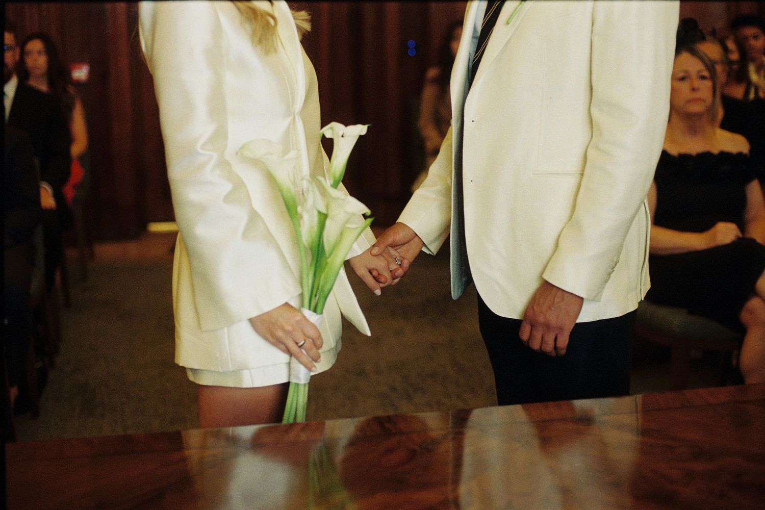 Bride and groom holding hands at wedding altar, bride holding white calla lily bouquet, both wearing ivory formal attire.