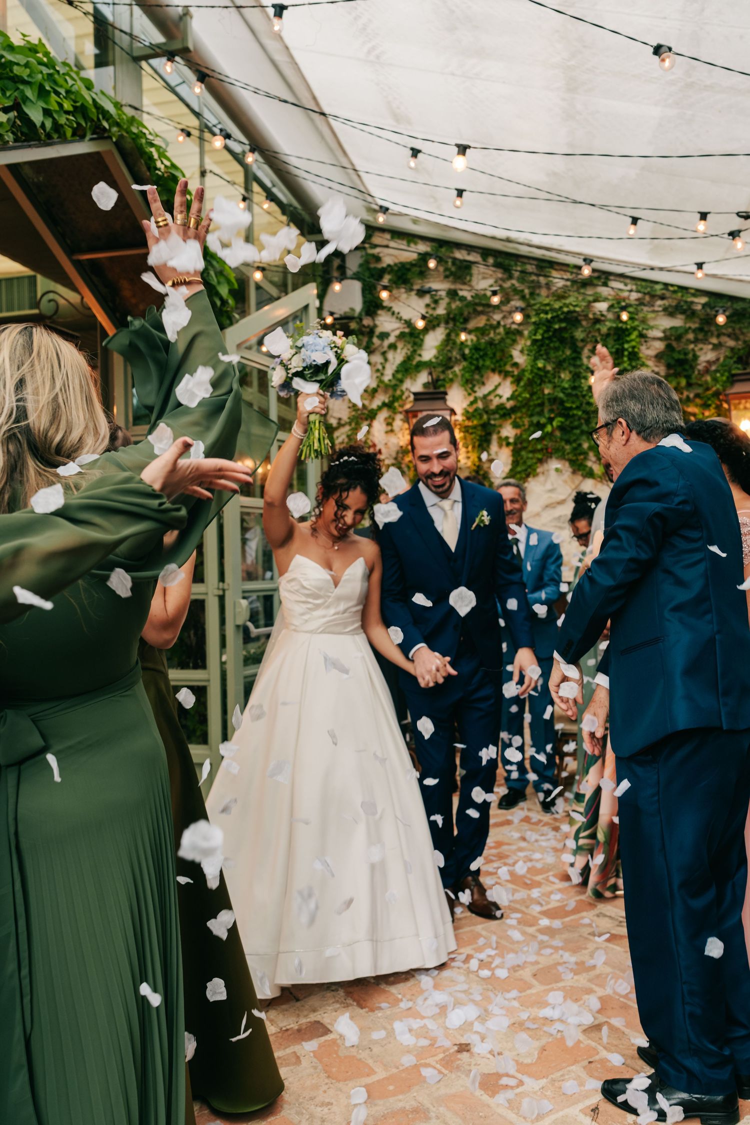 Bride and groom walk through confetti shower as guests celebrate their wedding ceremony exit.