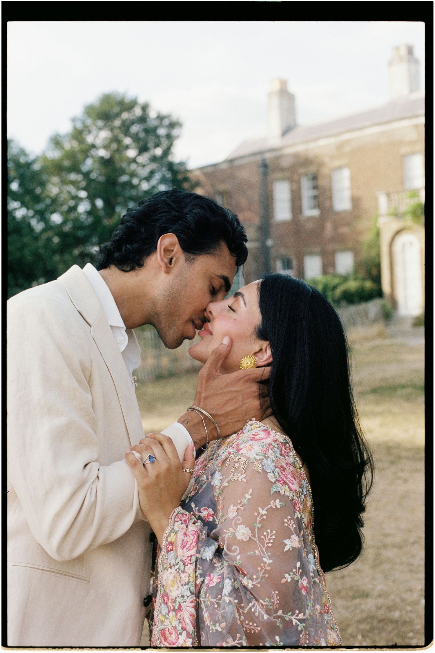 A couple shares a romantic kiss outdoors near a historic brick building during their engagement session.