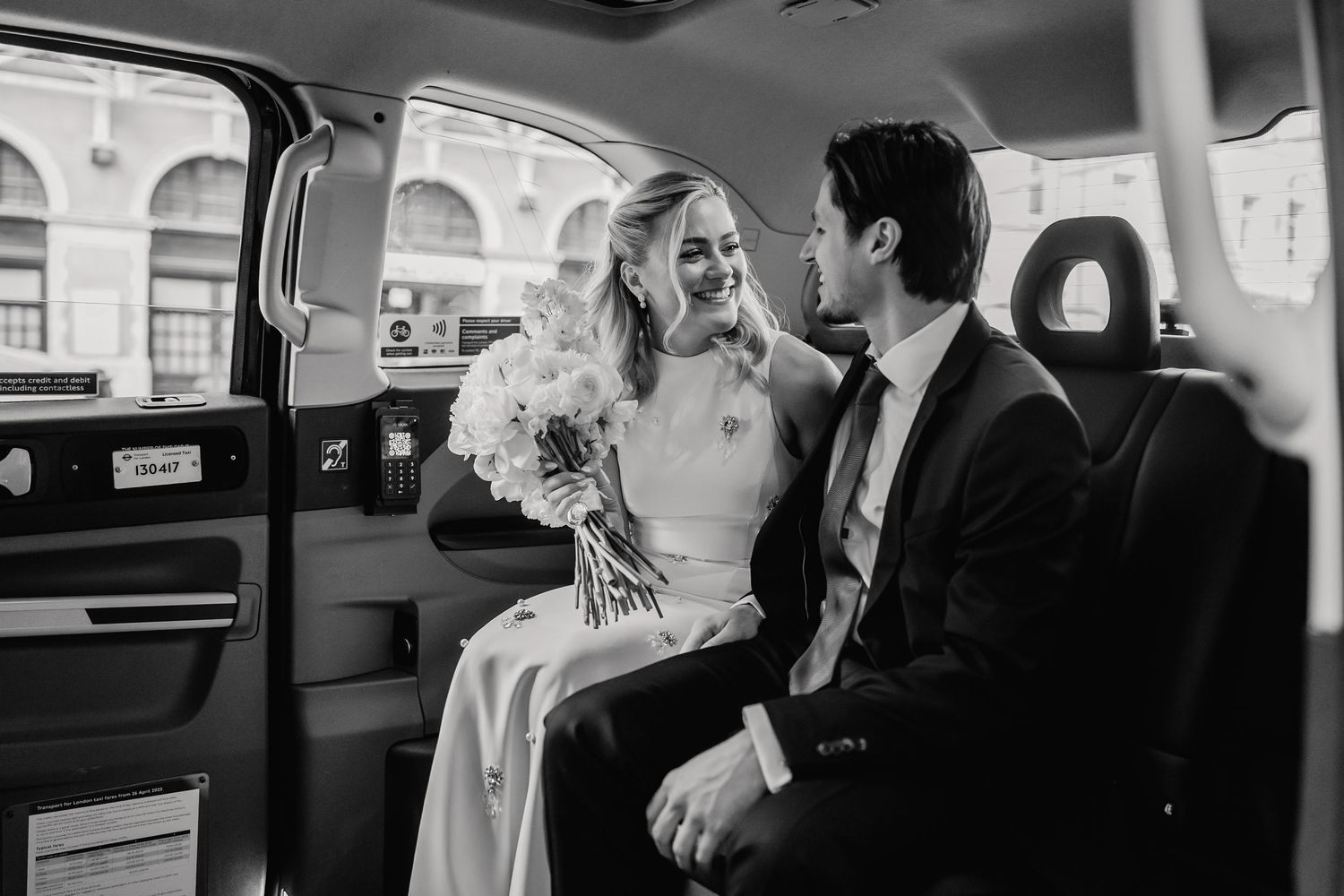 Bride and groom share a joyful moment in a black London taxi cab on their wedding day.