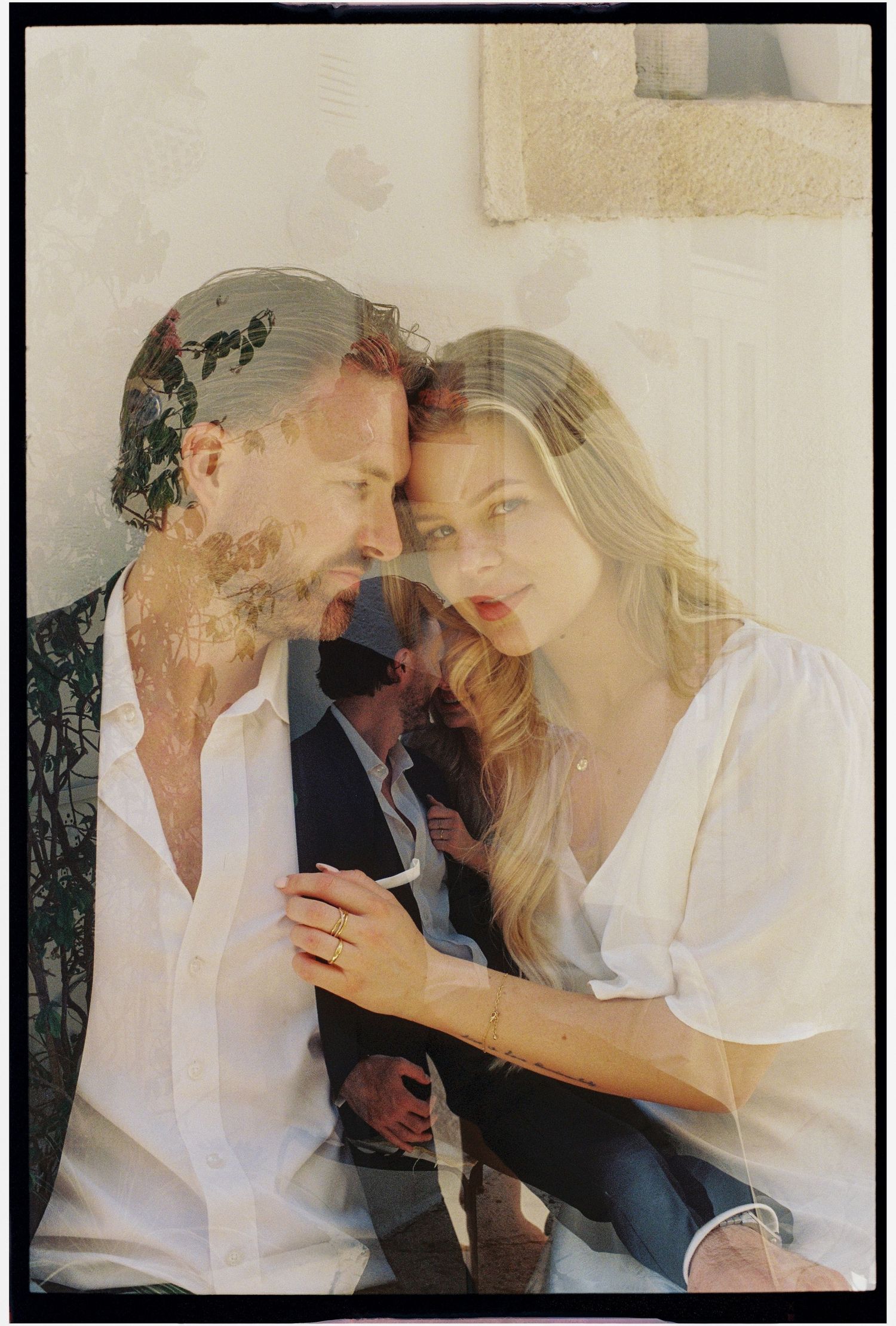 A romantic couple in white outfits share an intimate moment, captured in a dreamy double exposure film photograph.