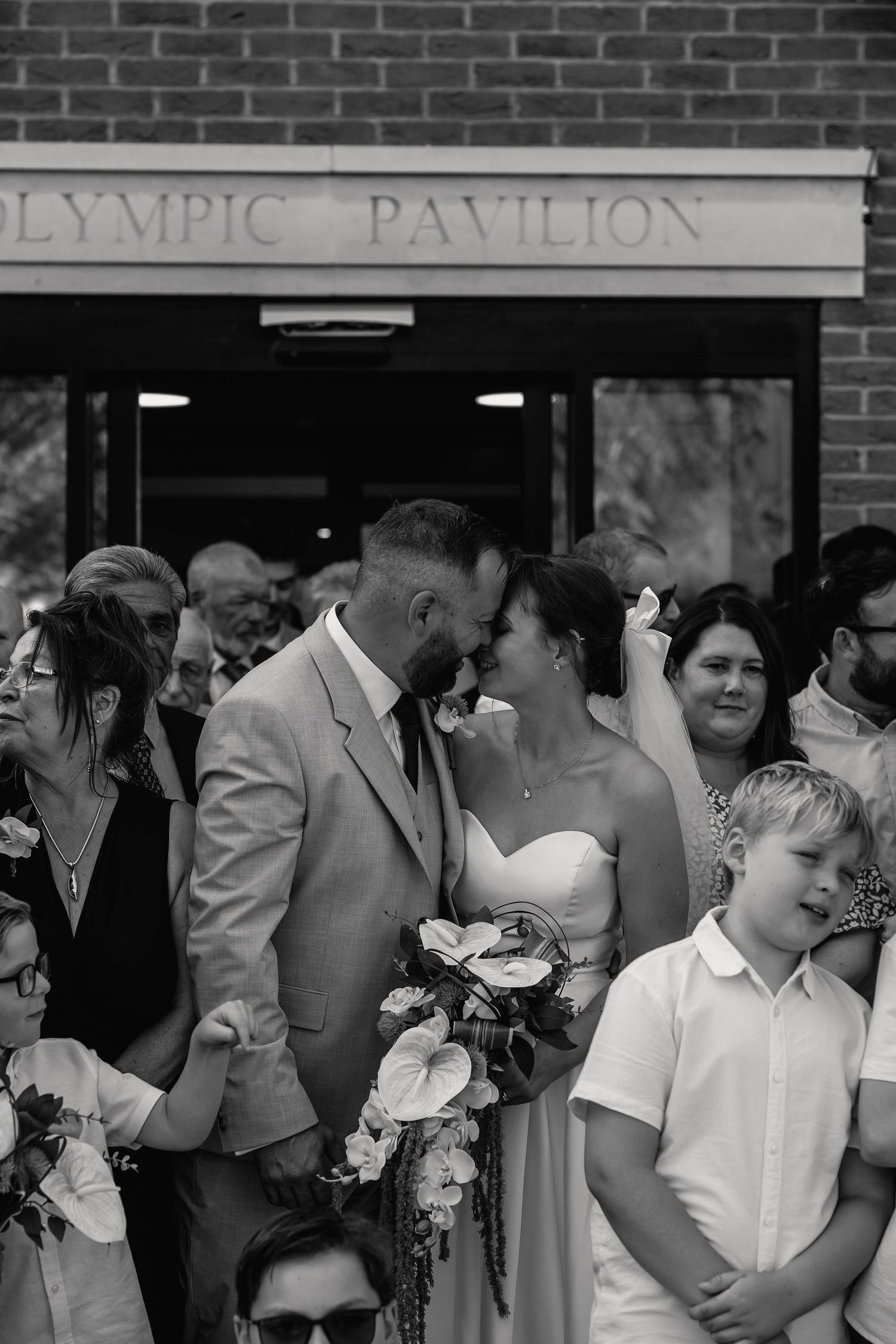 Black and white photo of a couple sharing a kiss outside the Olympic Pavilion on their wedding day.