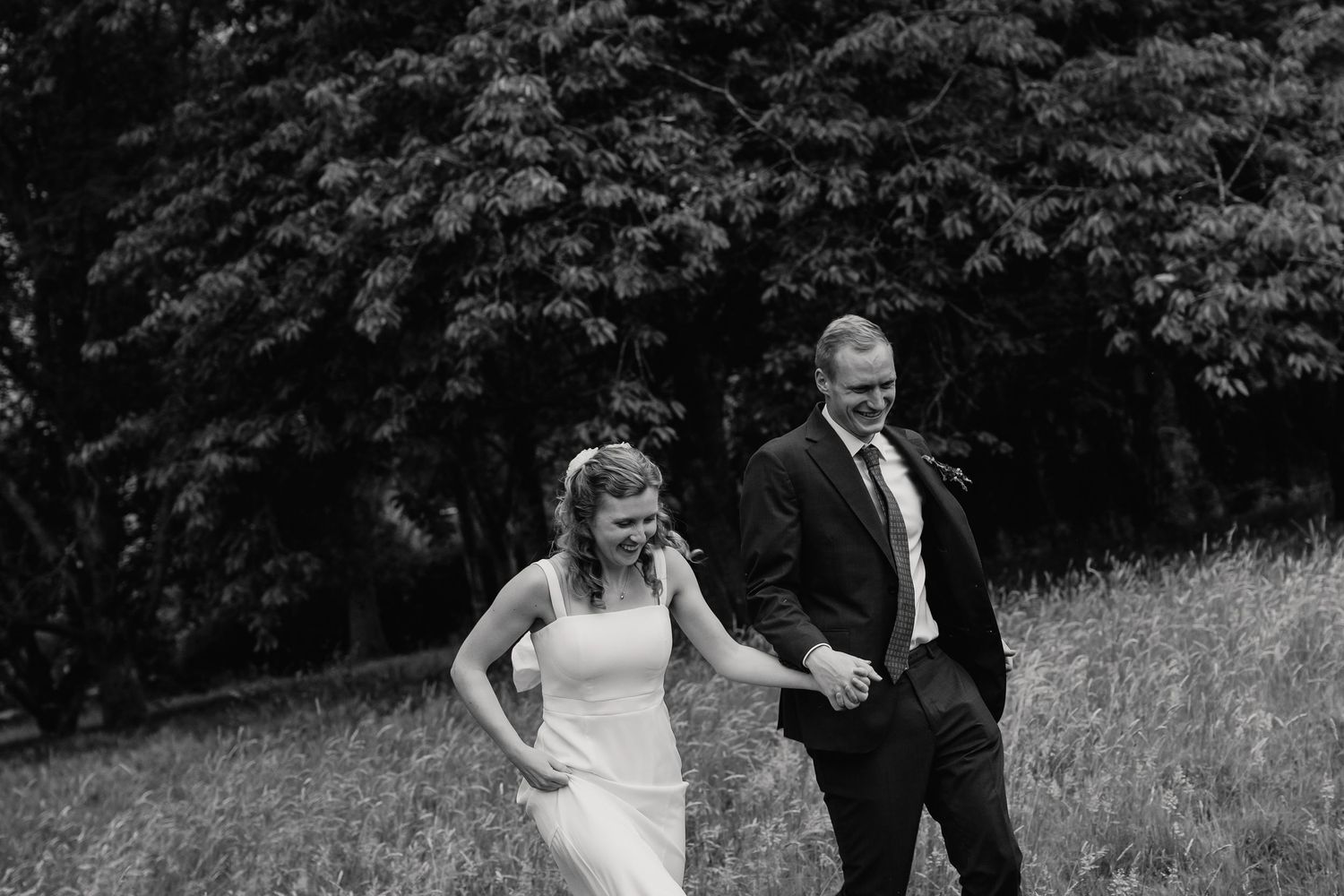 Black and white photo of happy couple running through a lush green meadow together.
