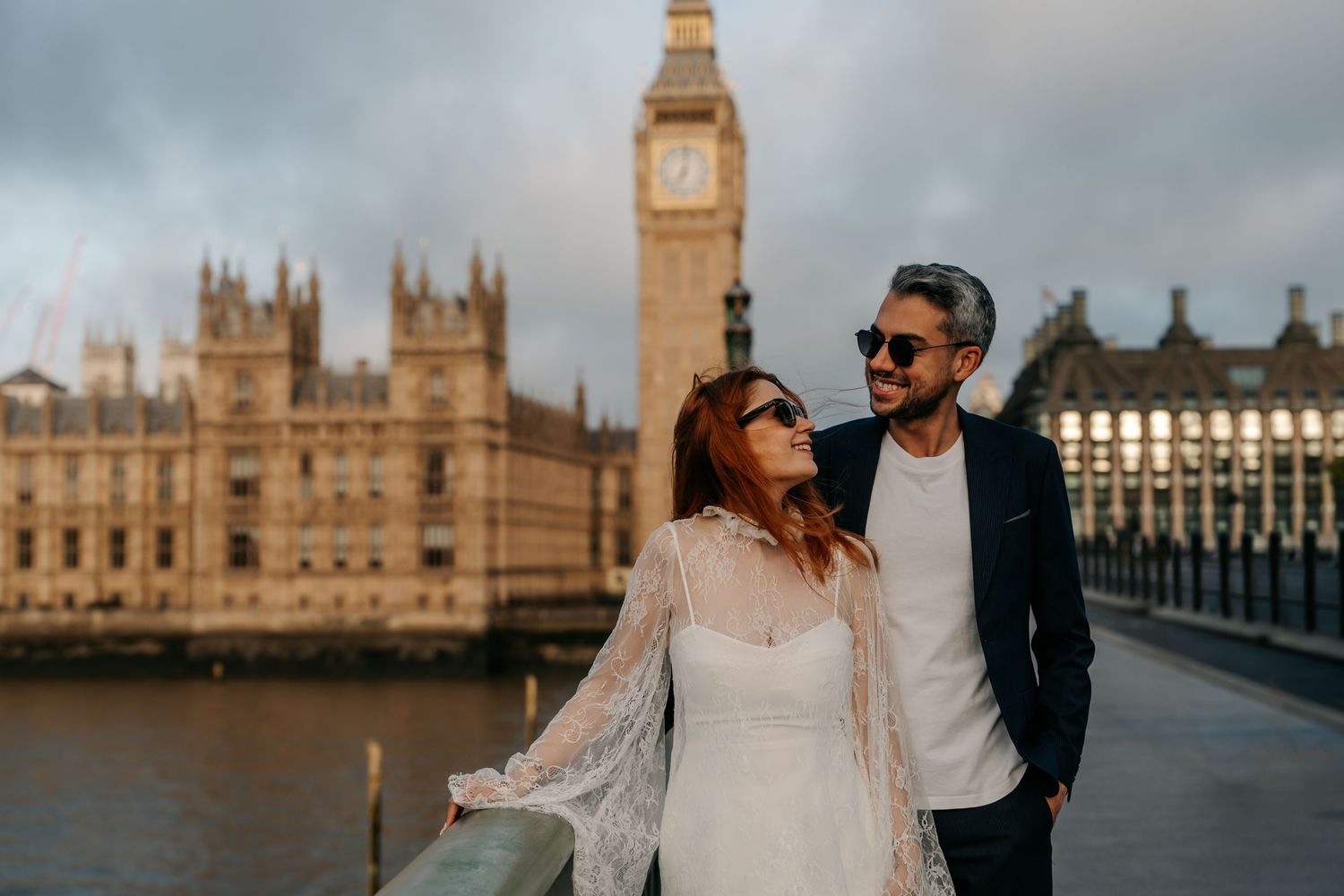 Couple posing on Westminster Bridge with Big Ben and Houses of Parliament in London backdrop at dusk.