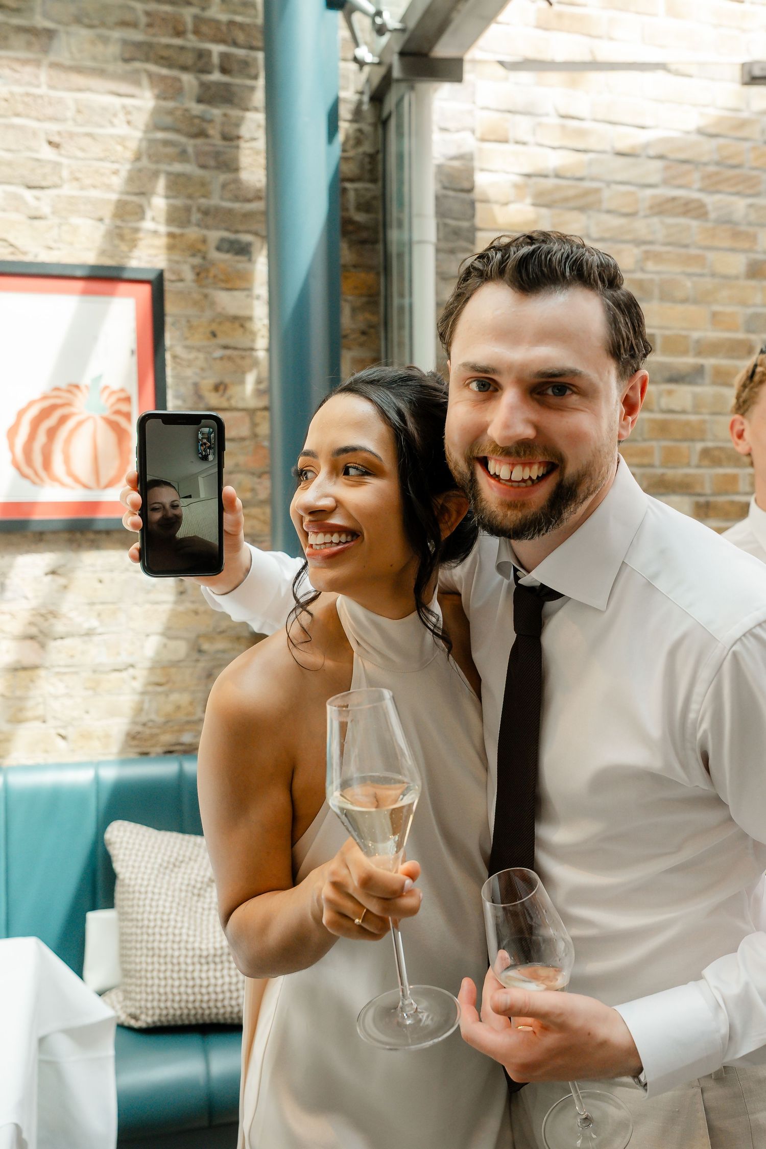 Bride and groom smiling while taking a selfie together holding champagne glasses at their reception.