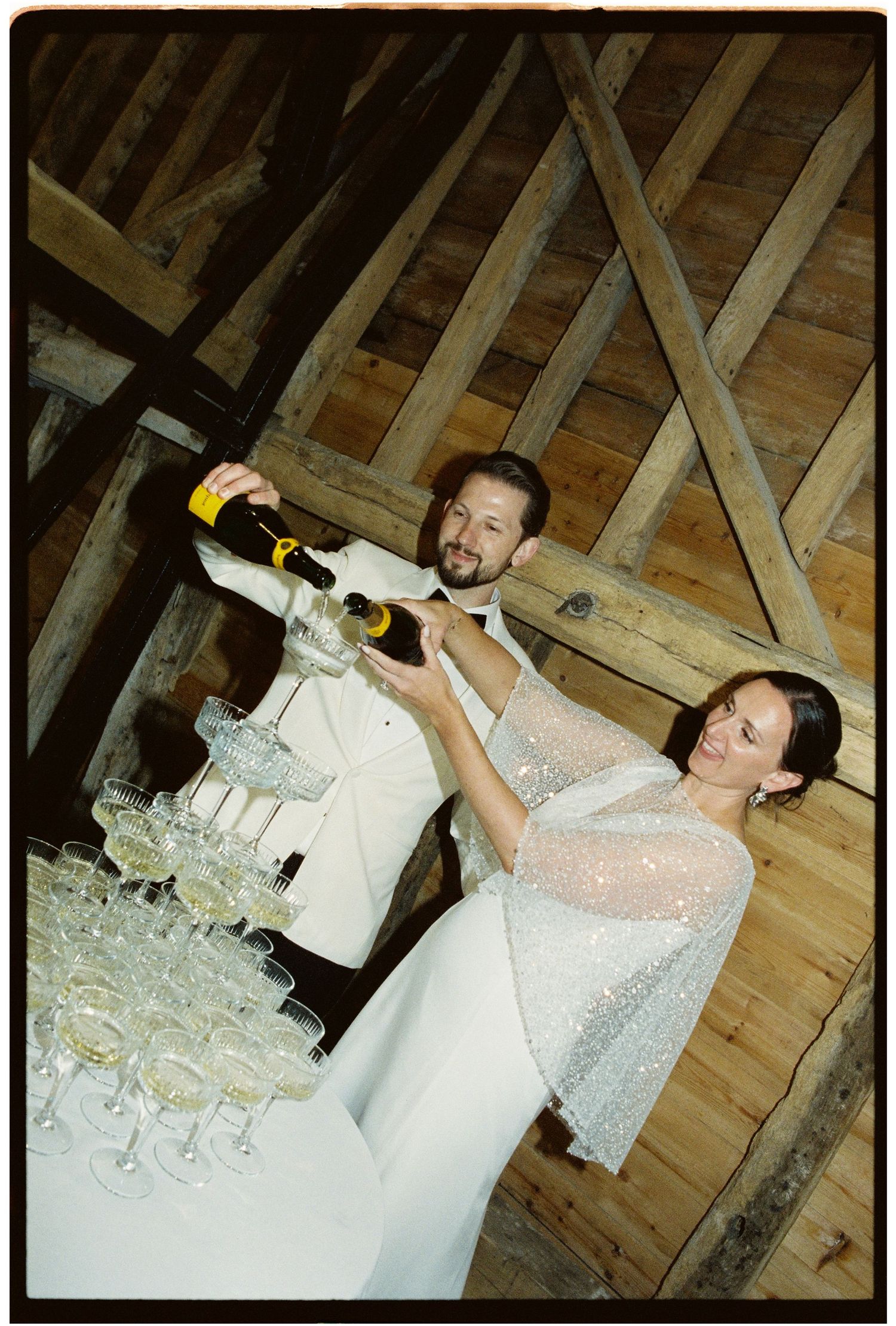 Bride and groom pour champagne tower at rustic barn wedding reception venue.