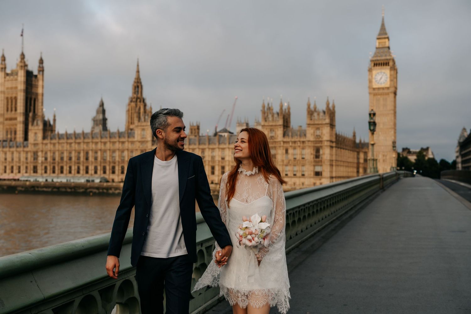Couple walking hand in hand on Westminster Bridge with Big Ben and Houses of Parliament in London backdrop.
