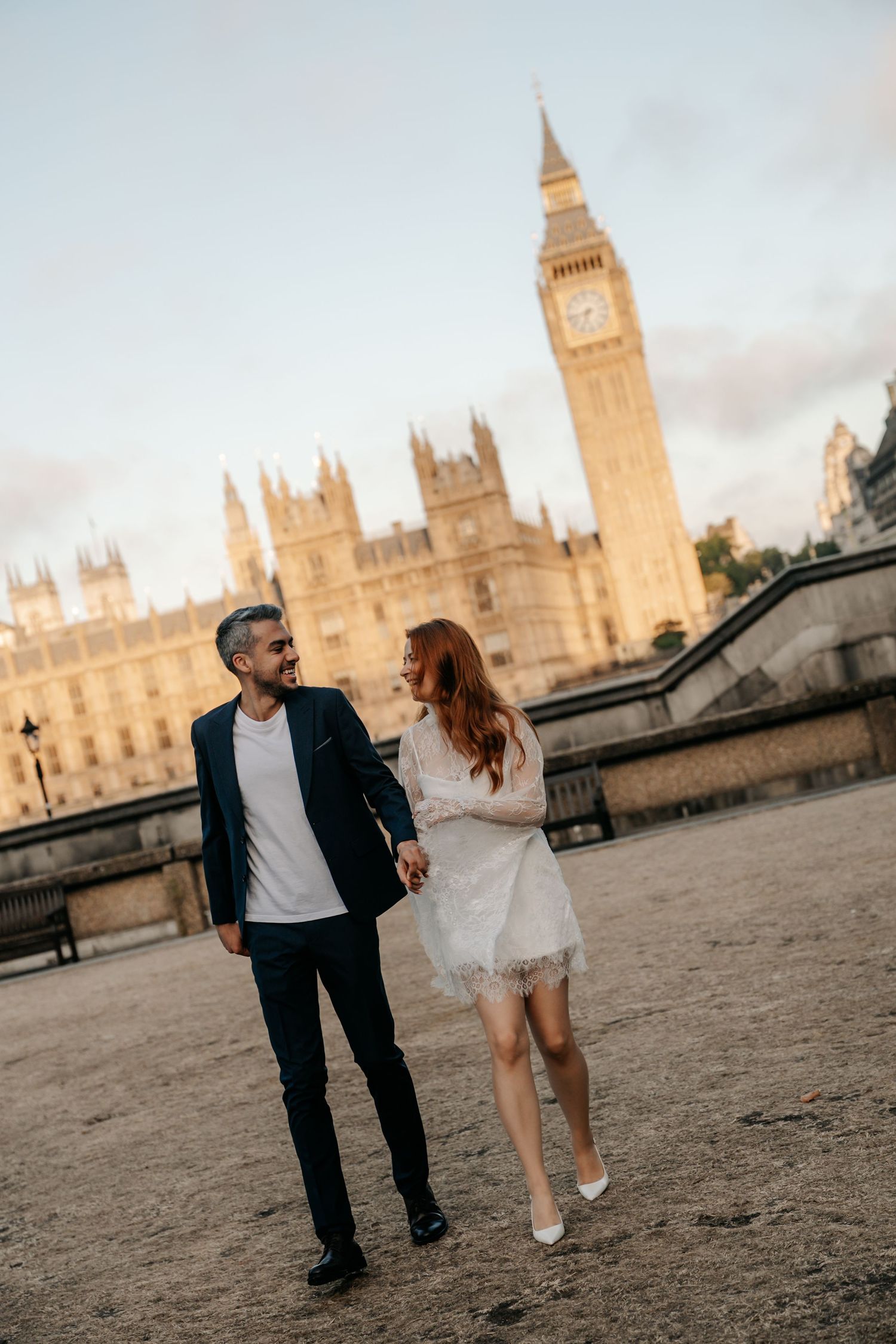 Couple holding hands walking near Big Ben and Houses of Parliament in London at golden hour.