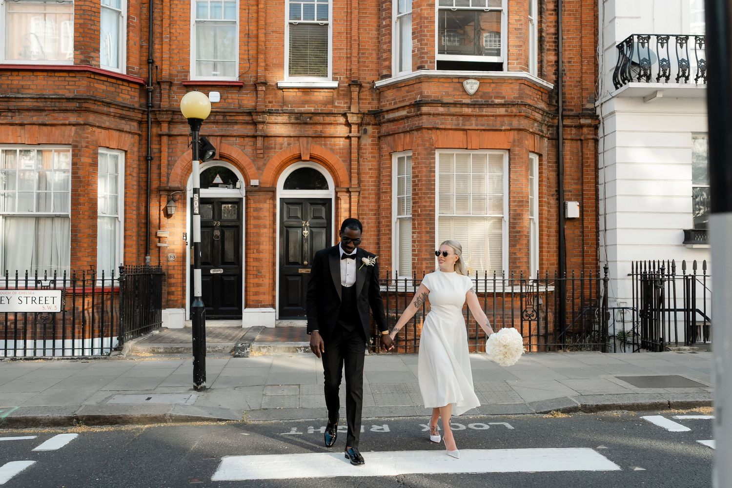 Stylish newlywed couple crossing a zebra crossing in front of a classic London brick building.