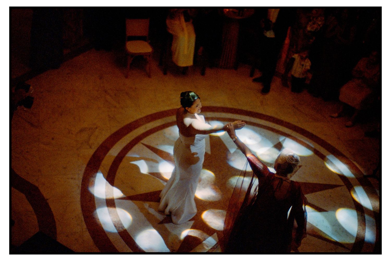 Aerial view of bride and groom sharing first dance on ornate illuminated ballroom floor.