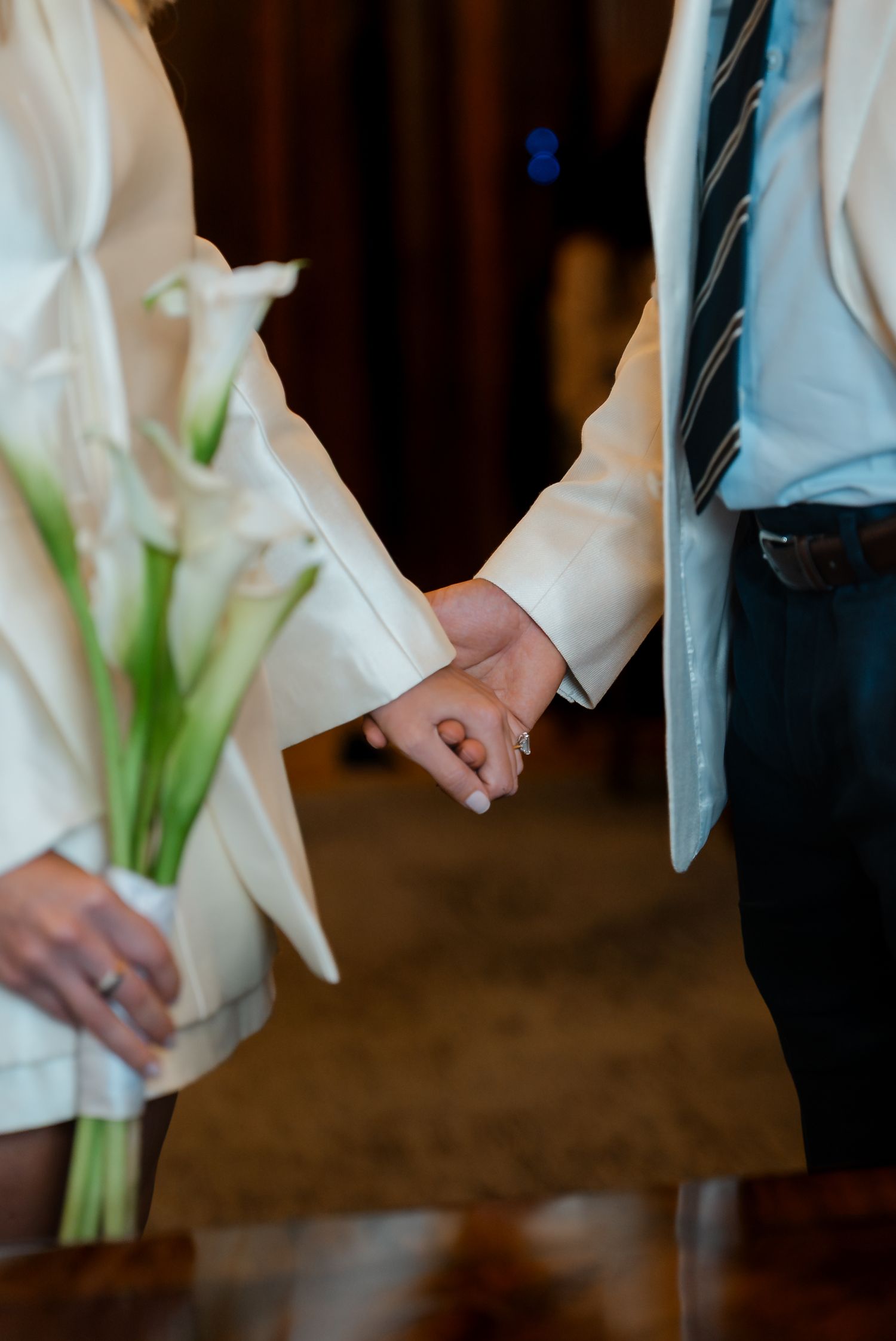 Bride and groom holding hands, bride carrying white calla lily bouquet at wedding ceremony.