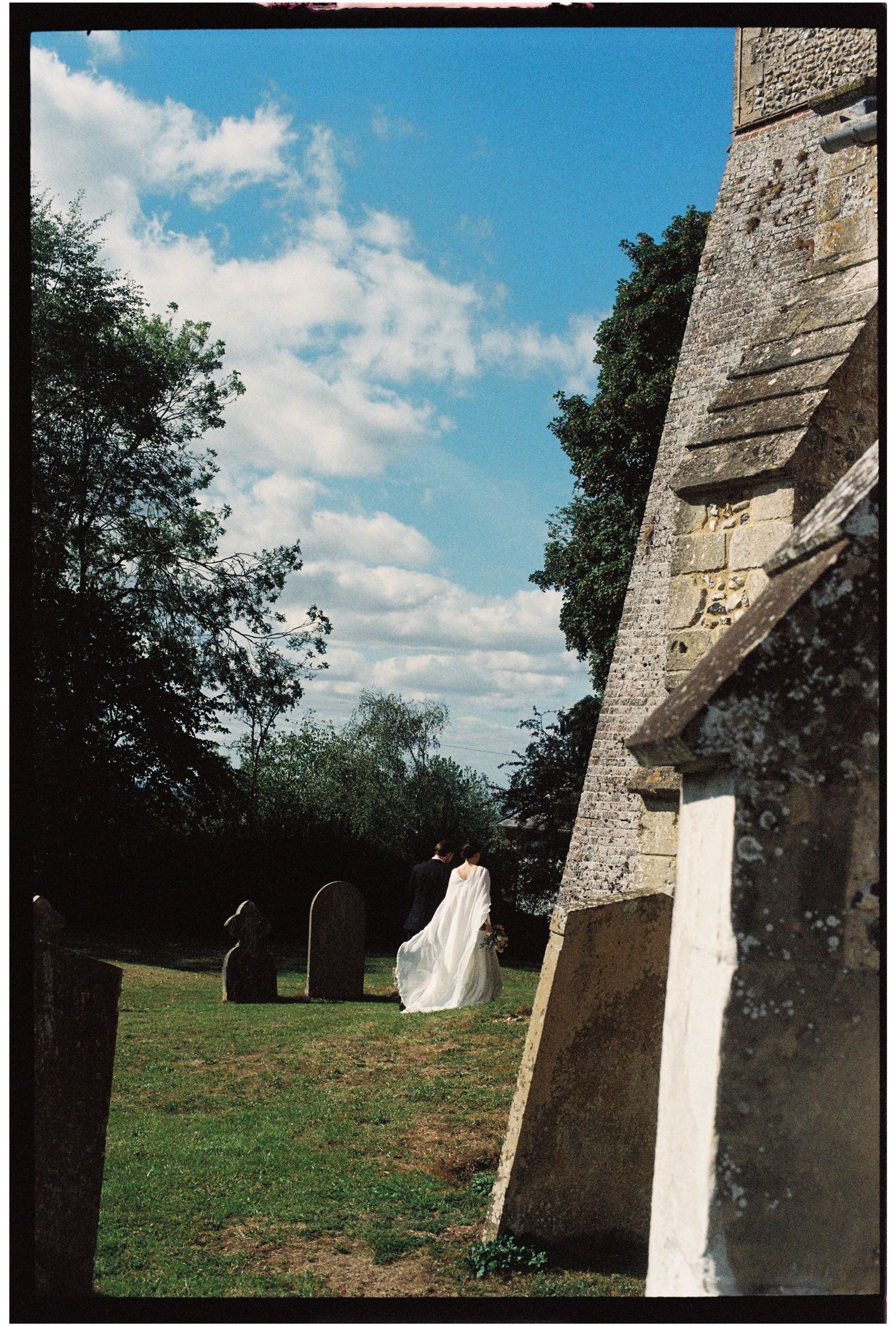 A ghostly white figure walks among old gravestones beside a stone church tower under a blue sky.