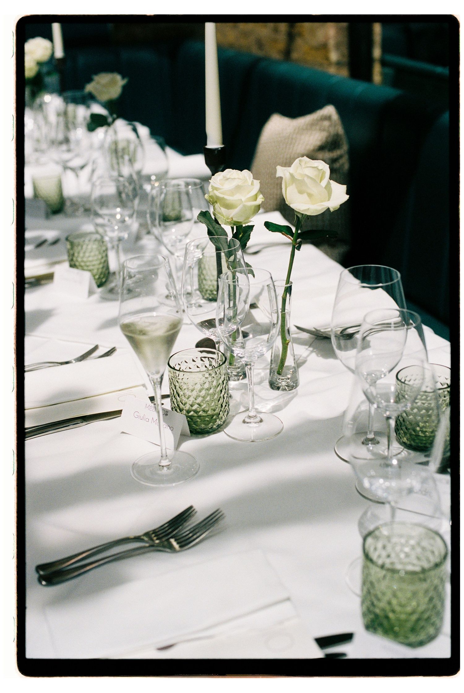 Elegant wedding table setting with white roses in bud vases, green textured glasses and candlesticks.