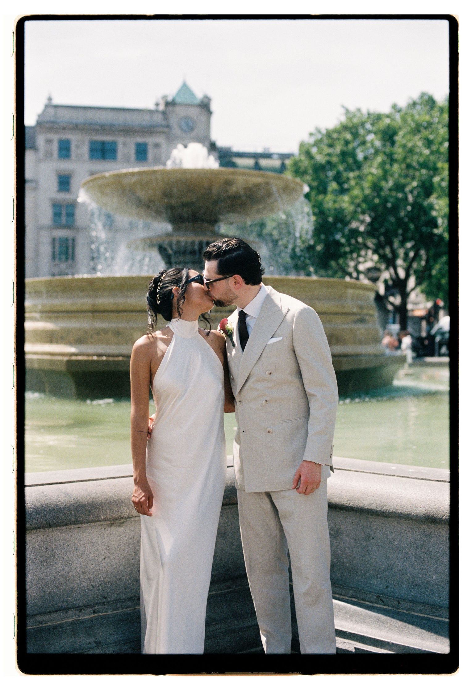 Bride and groom sharing a kiss in front of a fountain at Trafalgar Square on their wedding day.