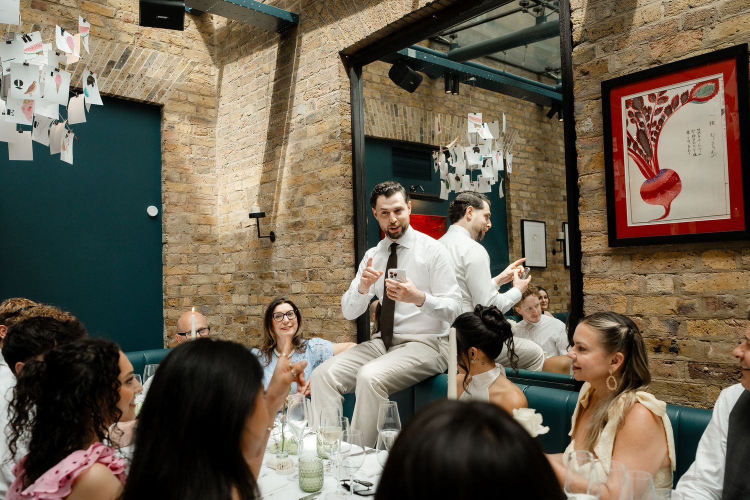 Groom giving a speech to seated wedding guests in a warmly lit rustic brick restaurant venue.