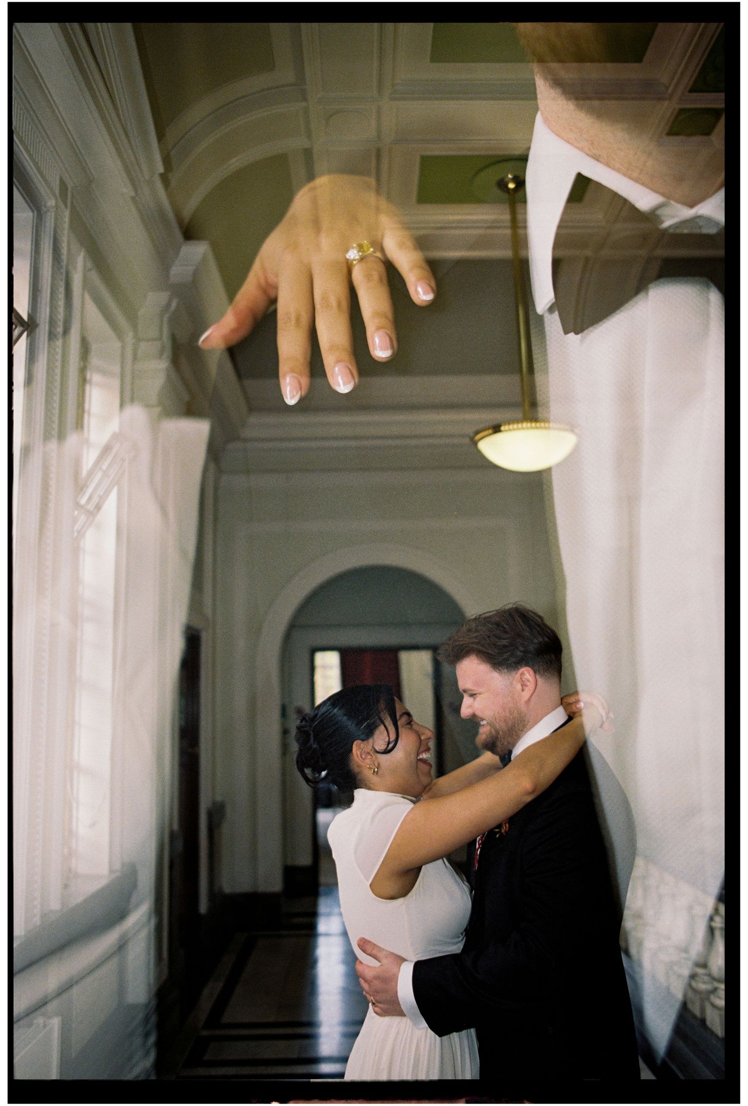 Couple embracing in elegant hallway with a close-up of a wedding ring hand overlay above them.