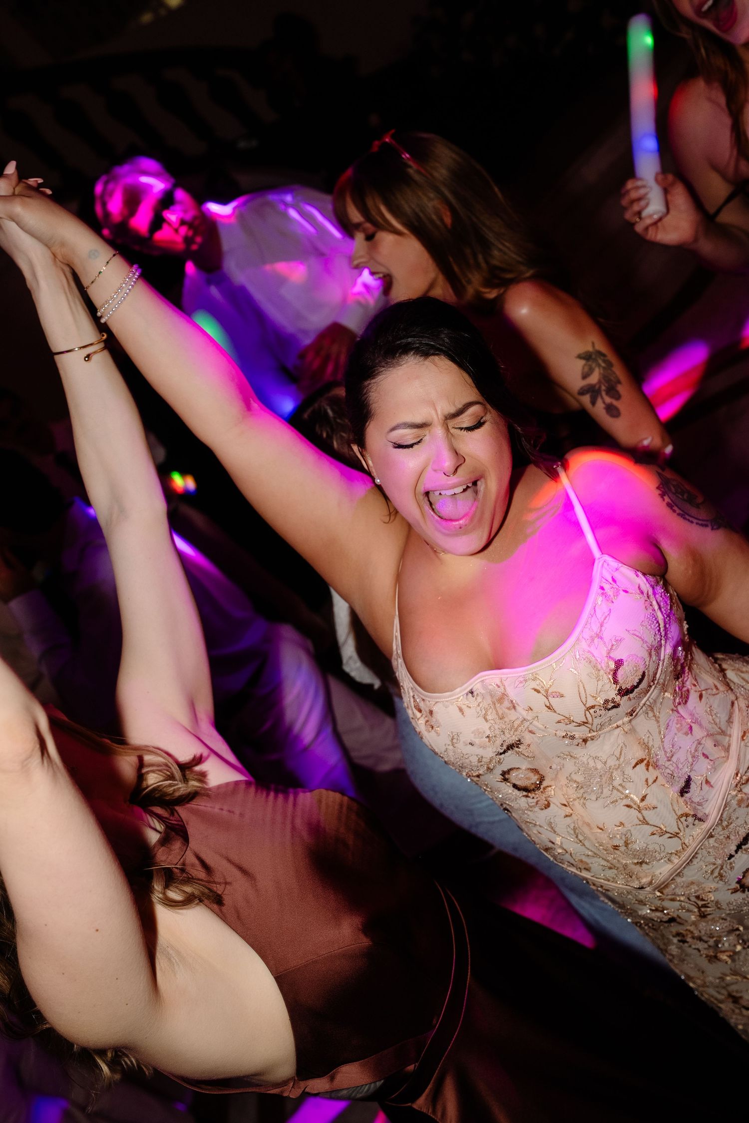 Woman in white dress dances energetically under pink lights at vibrant wedding reception party.