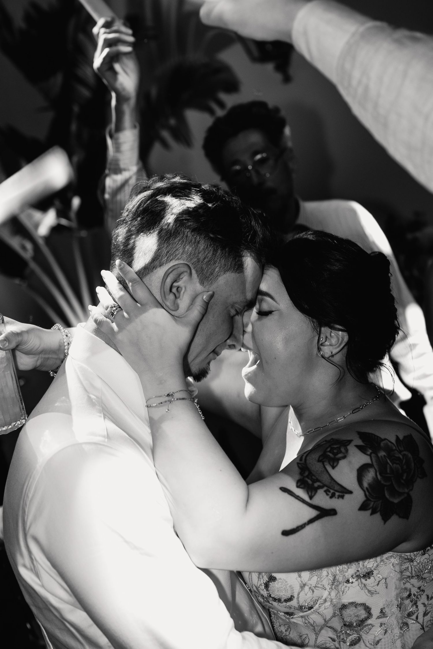 Bride and groom share tender forehead-to-forehead moment surrounded by guests in black and white.