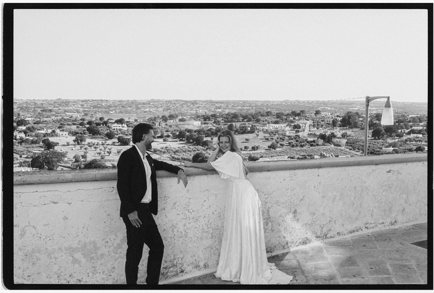 Bride and groom share romantic moment on rooftop terrace overlooking ancient Mediterranean cityscape.