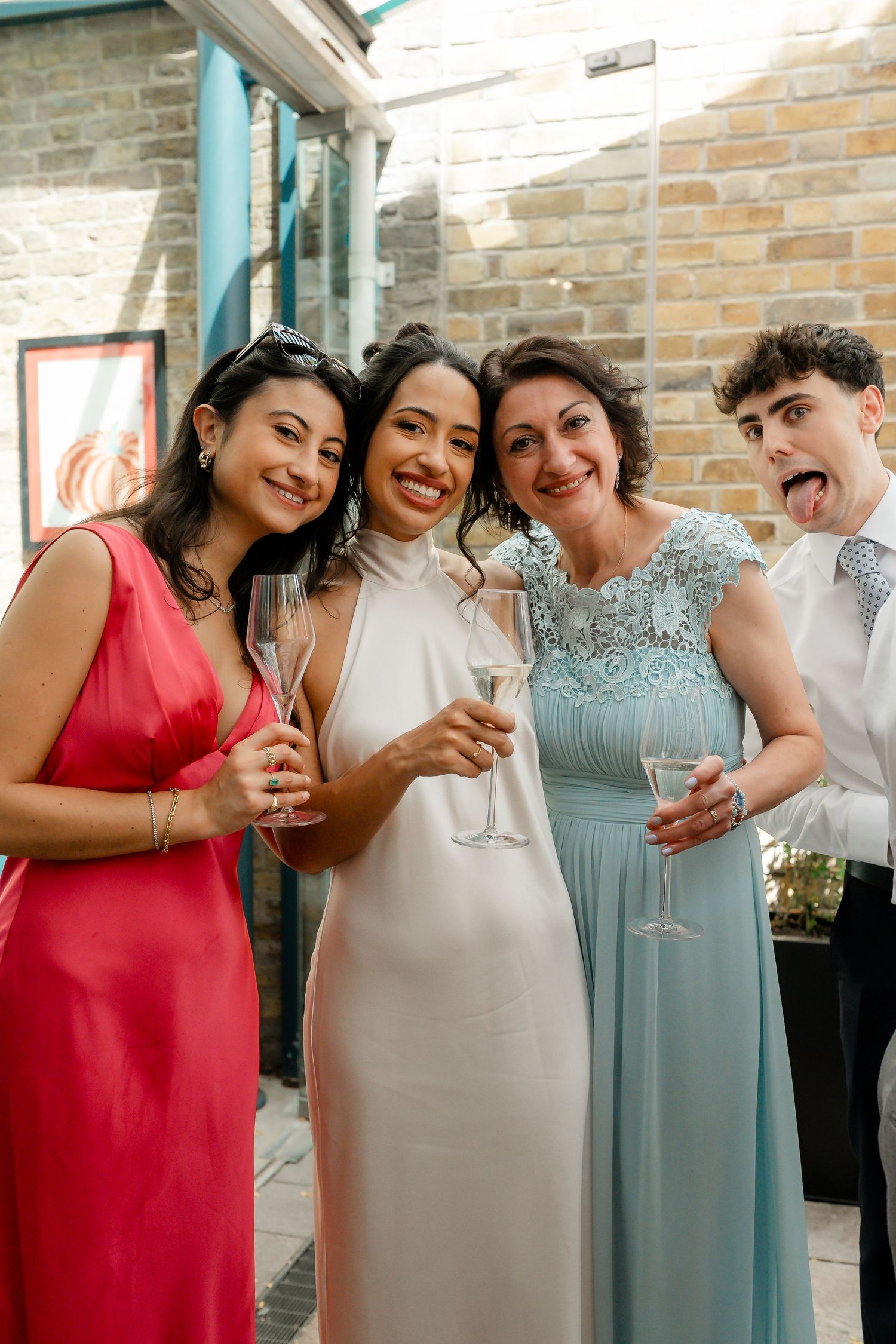 Bride posing with three smiling guests holding champagne flutes at a sunny outdoor wedding reception.