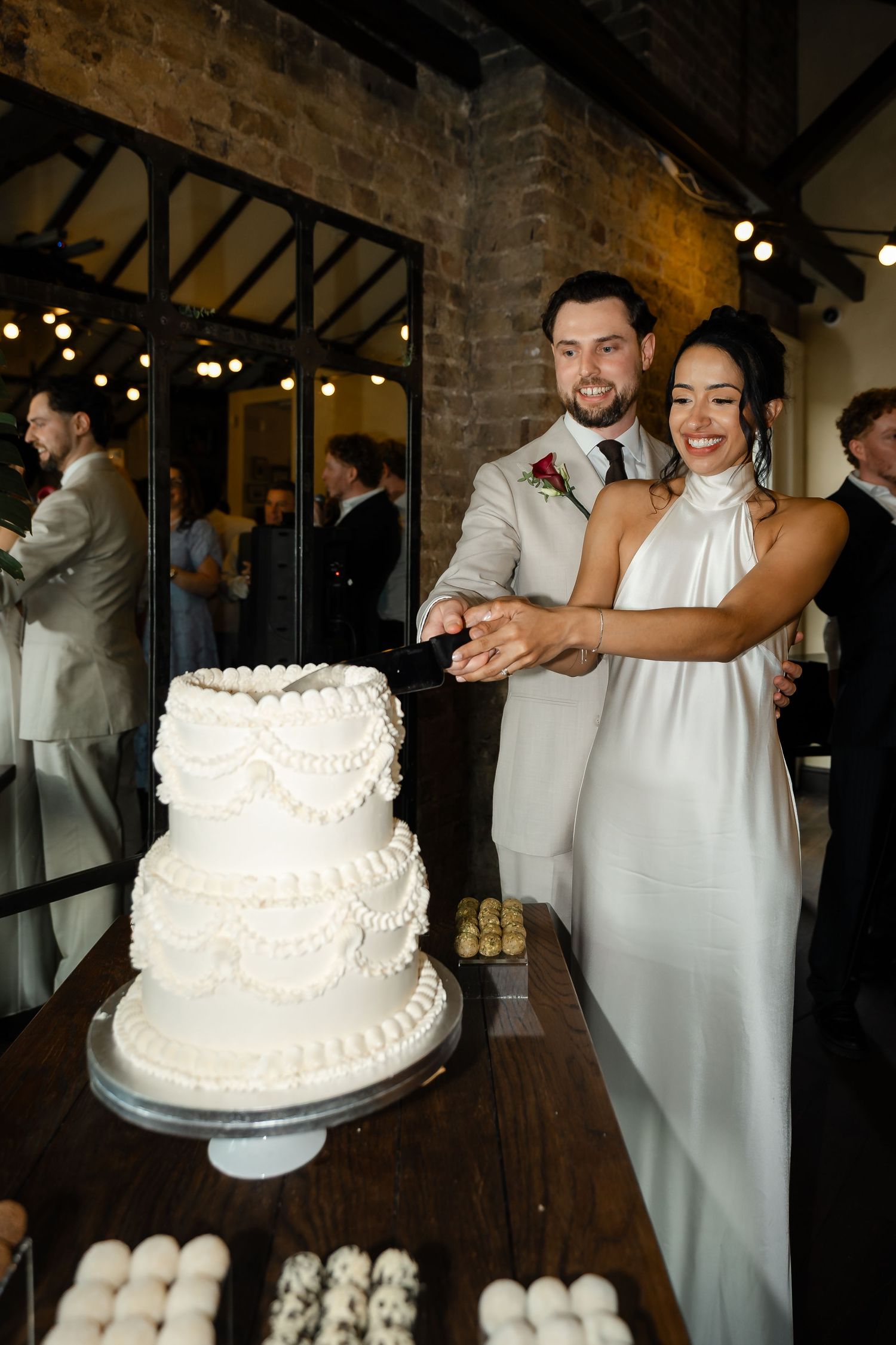 Smiling bride and groom cut their elegant three-tier white wedding cake at their reception.