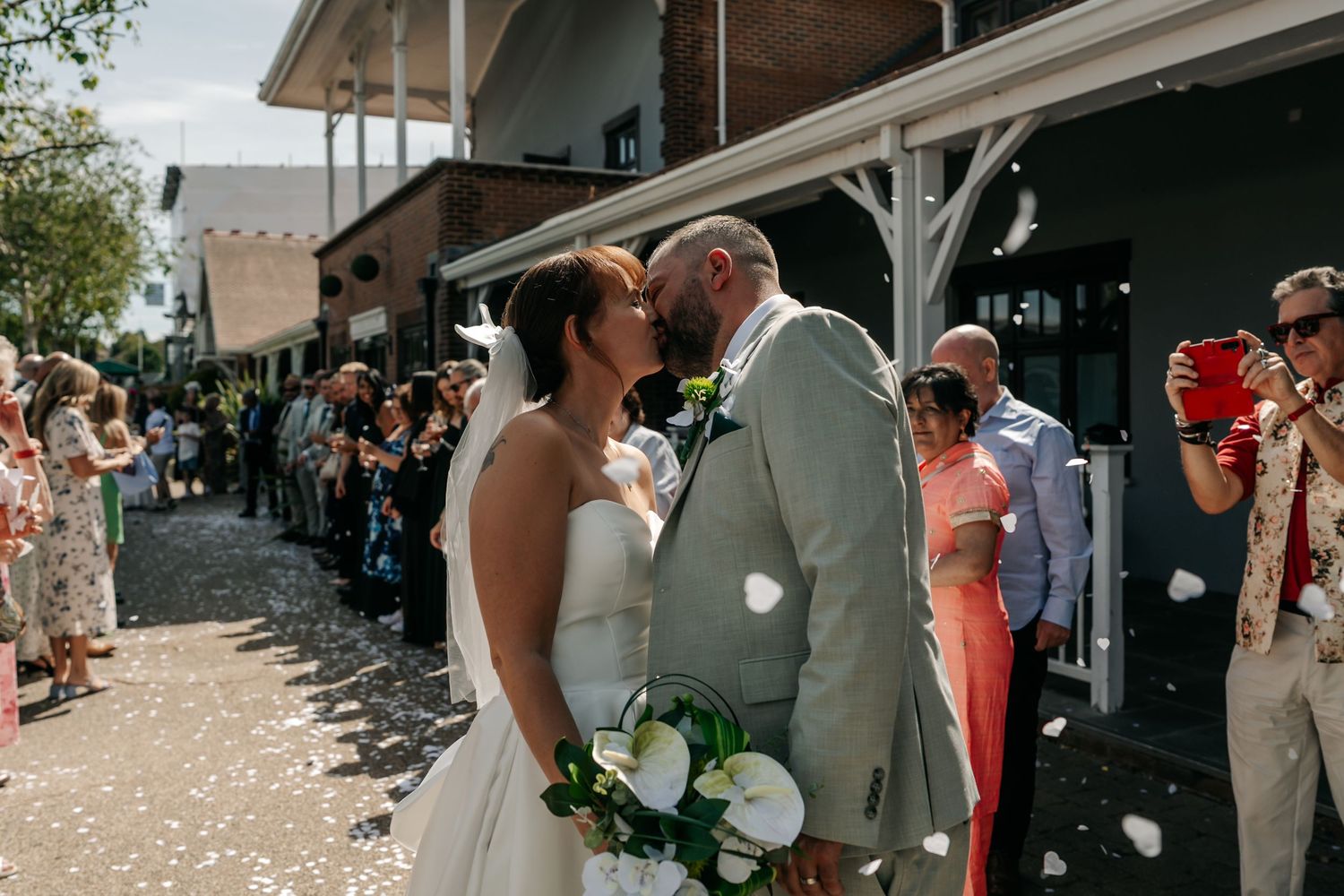 Newlywed couple sharing a kiss while guests throw confetti outside a venue on their wedding day.