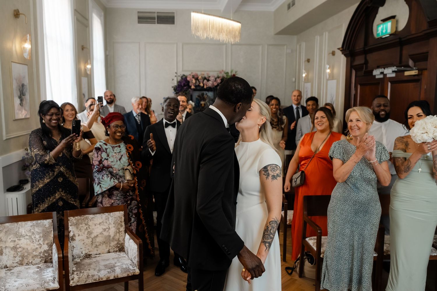 Newlyweds sharing their first kiss at the altar surrounded by joyful wedding guests.