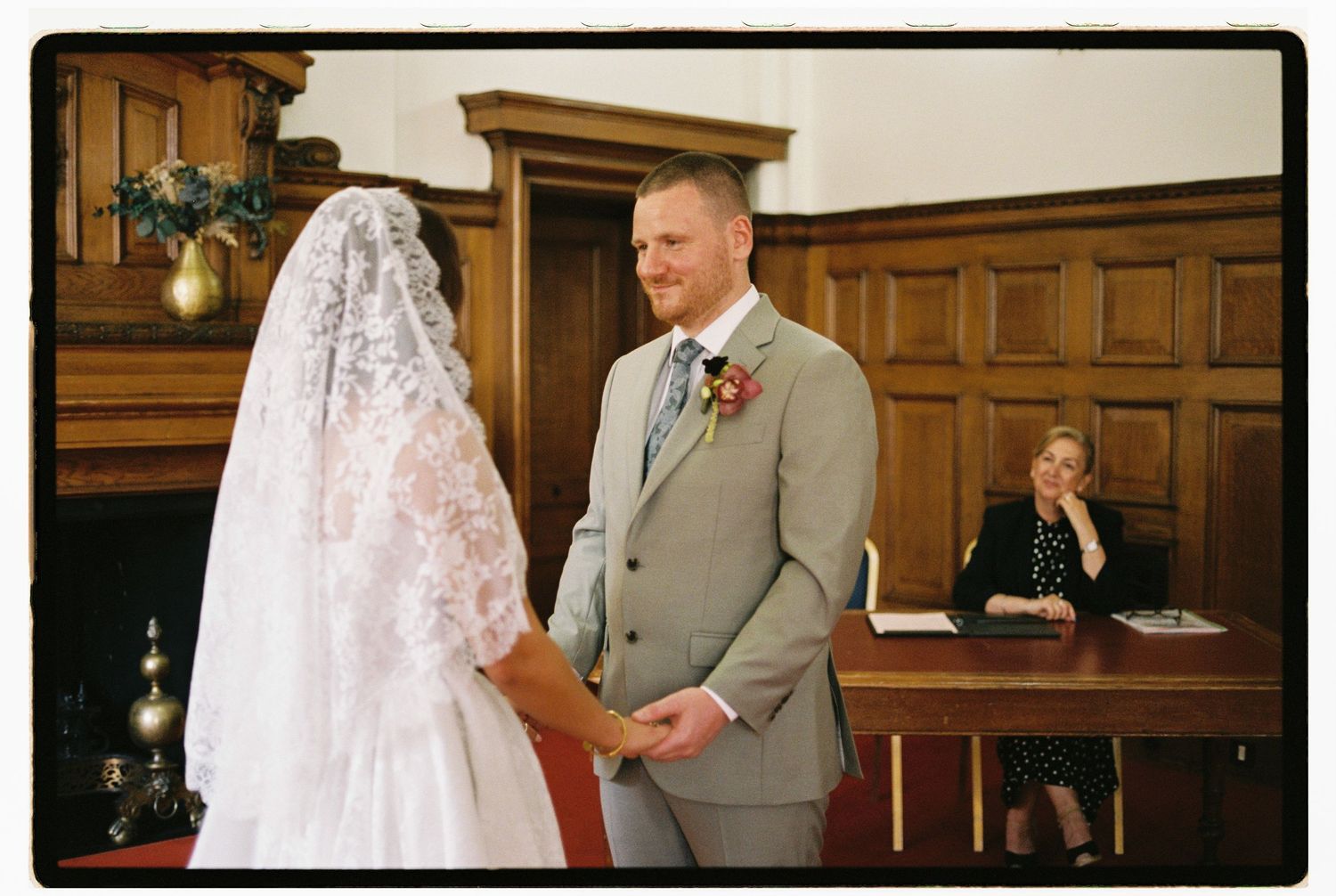 Bride and groom exchange vows at elegant wood-paneled wedding ceremony with officiant seated at desk.