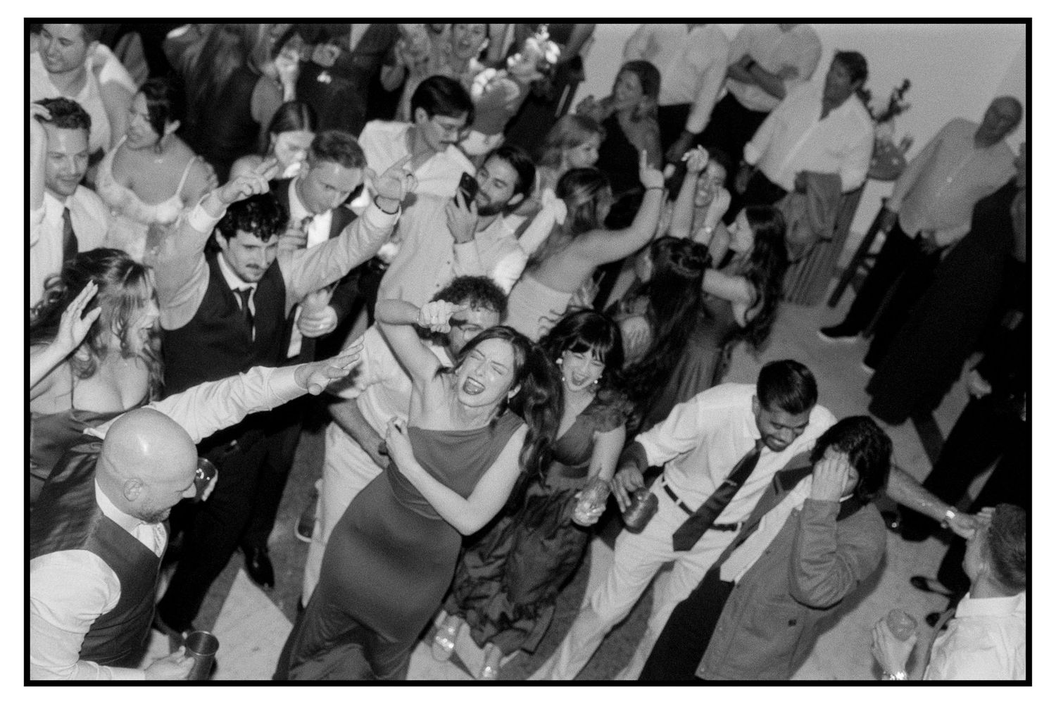 Black and white aerial view of wedding guests dancing and celebrating on a crowded dance floor.