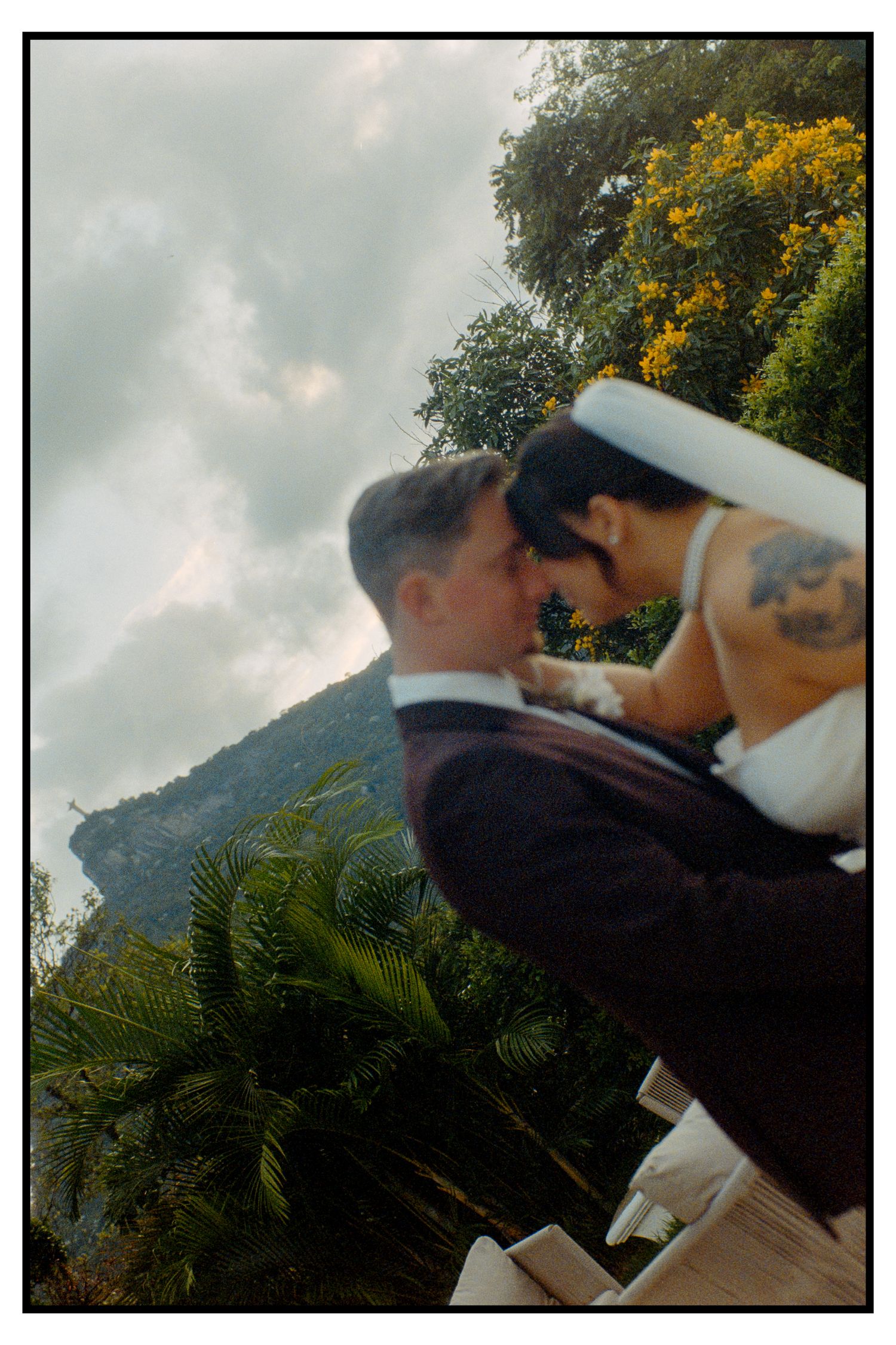 Bride and groom share an intimate moment outdoors with tropical greenery and mountains backdrop.