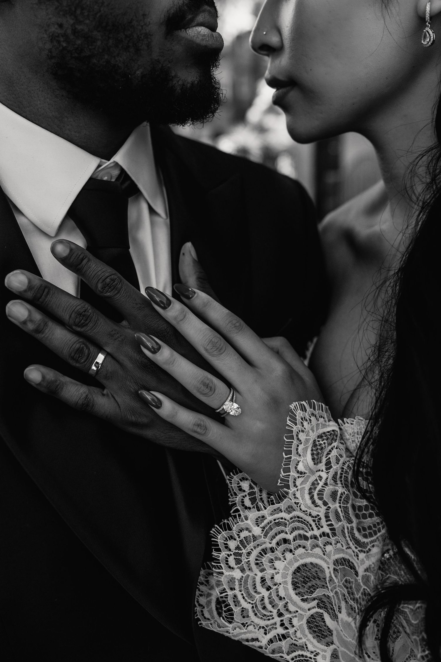A black and white close-up of an interracial couple nearly kissing, showcasing wedding and engagement rings.