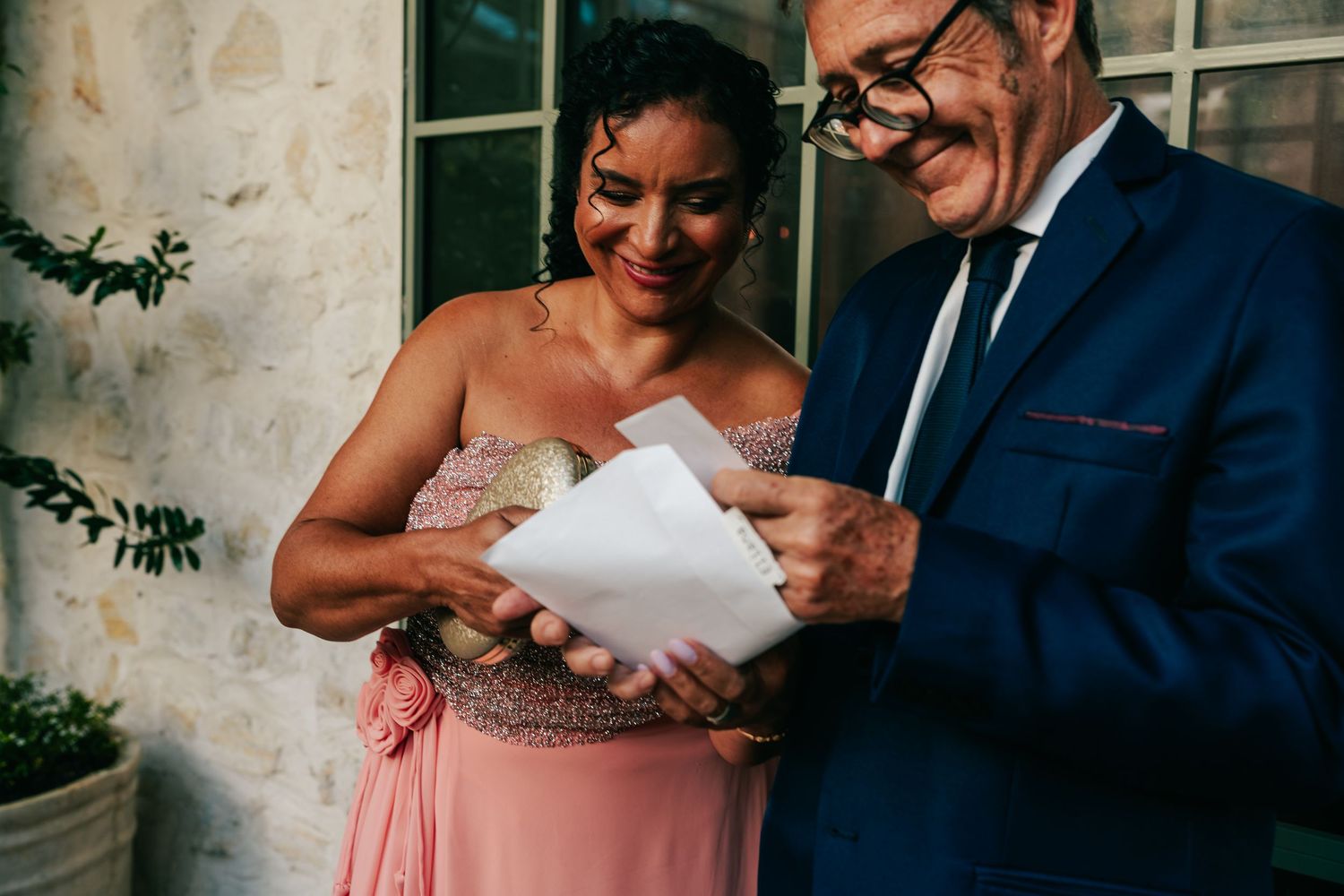 Woman in pink gown and man in navy suit share a joyful moment reading a letter.