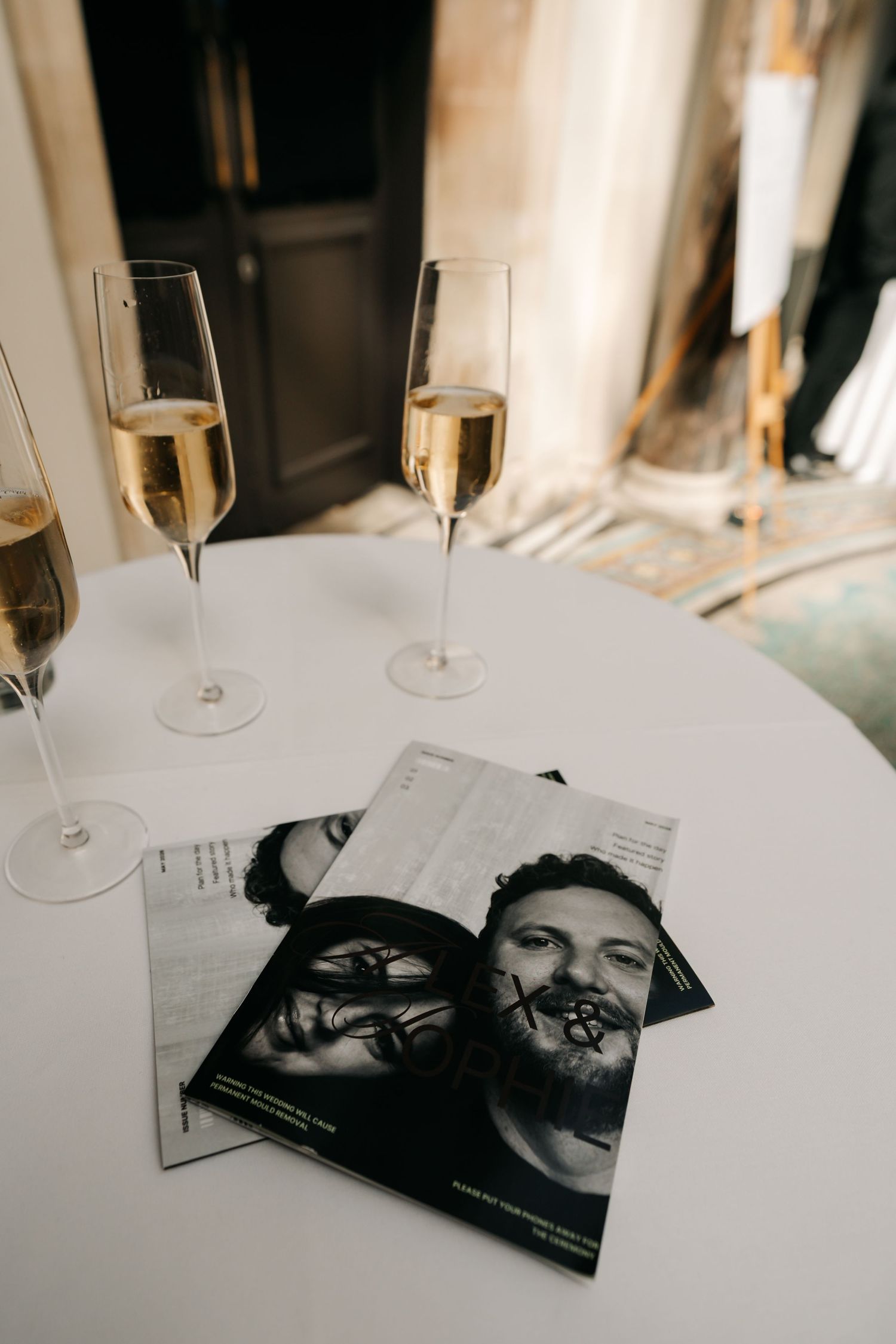 Champagne flutes and black-and-white wedding programs on a white table at reception.