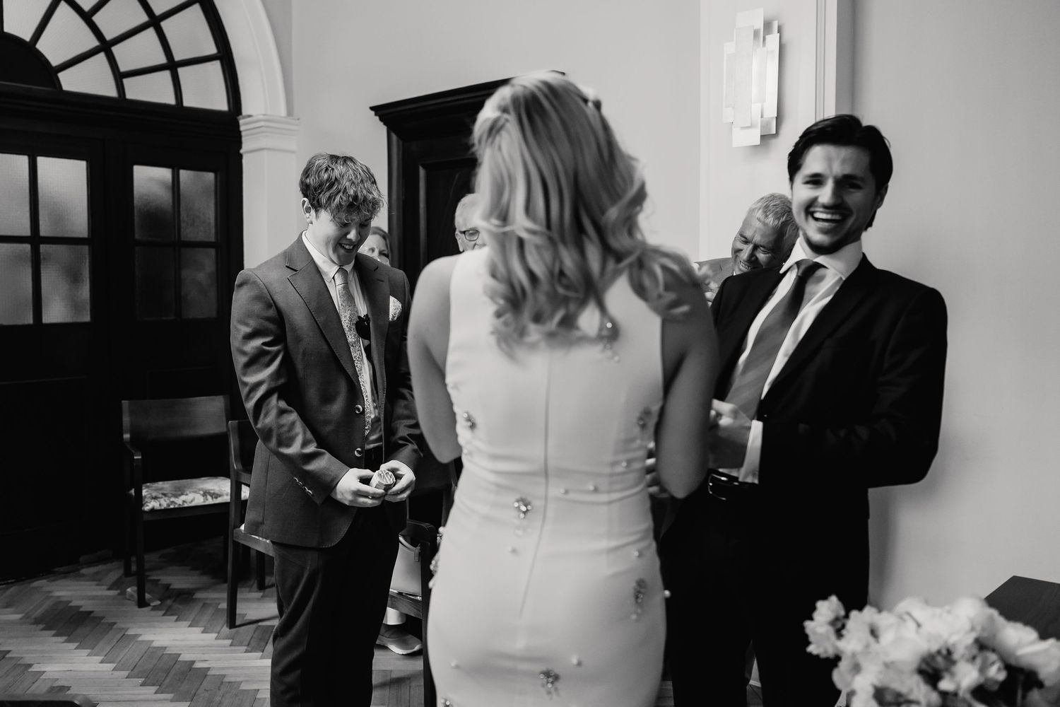 Bride in white dress laughs with smiling guest in black and white candid wedding reception photo.