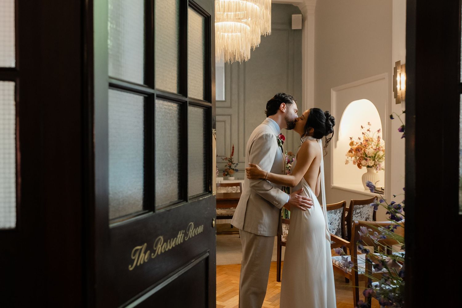 Romantic couple embracing and kissing inside elegant venue viewed through glass door of The Russell Room.