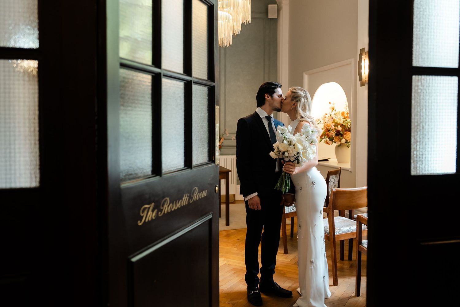 Couple shares romantic kiss framed by elegant dark doors of The Rosette Room.