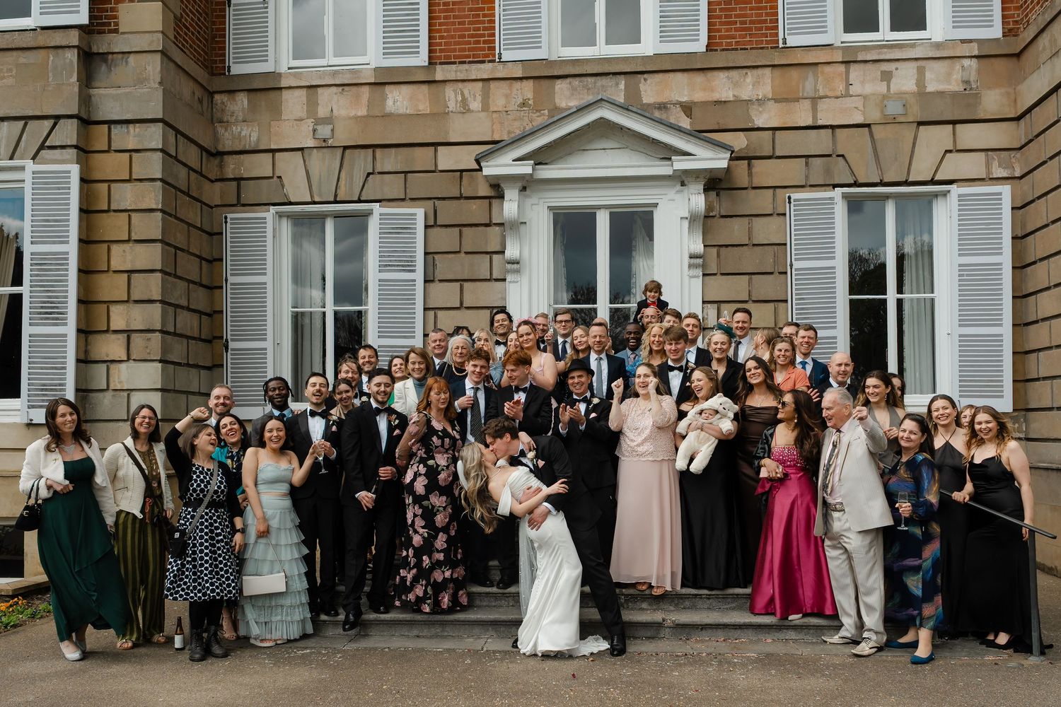 Large wedding party group photo outside elegant brick manor house venue.