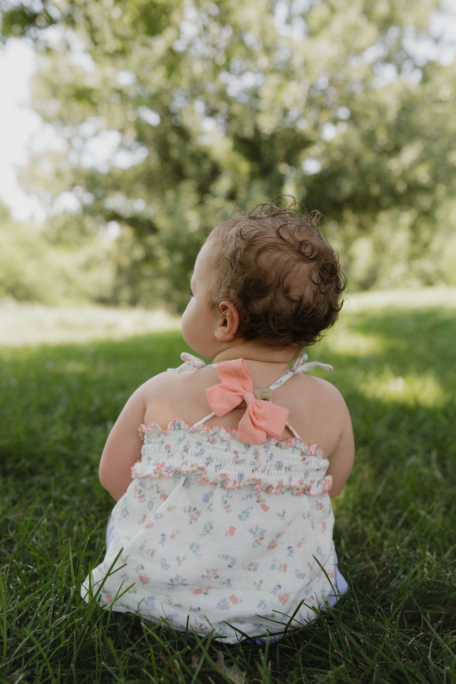 Toddler sitting in the grass looking at the trees